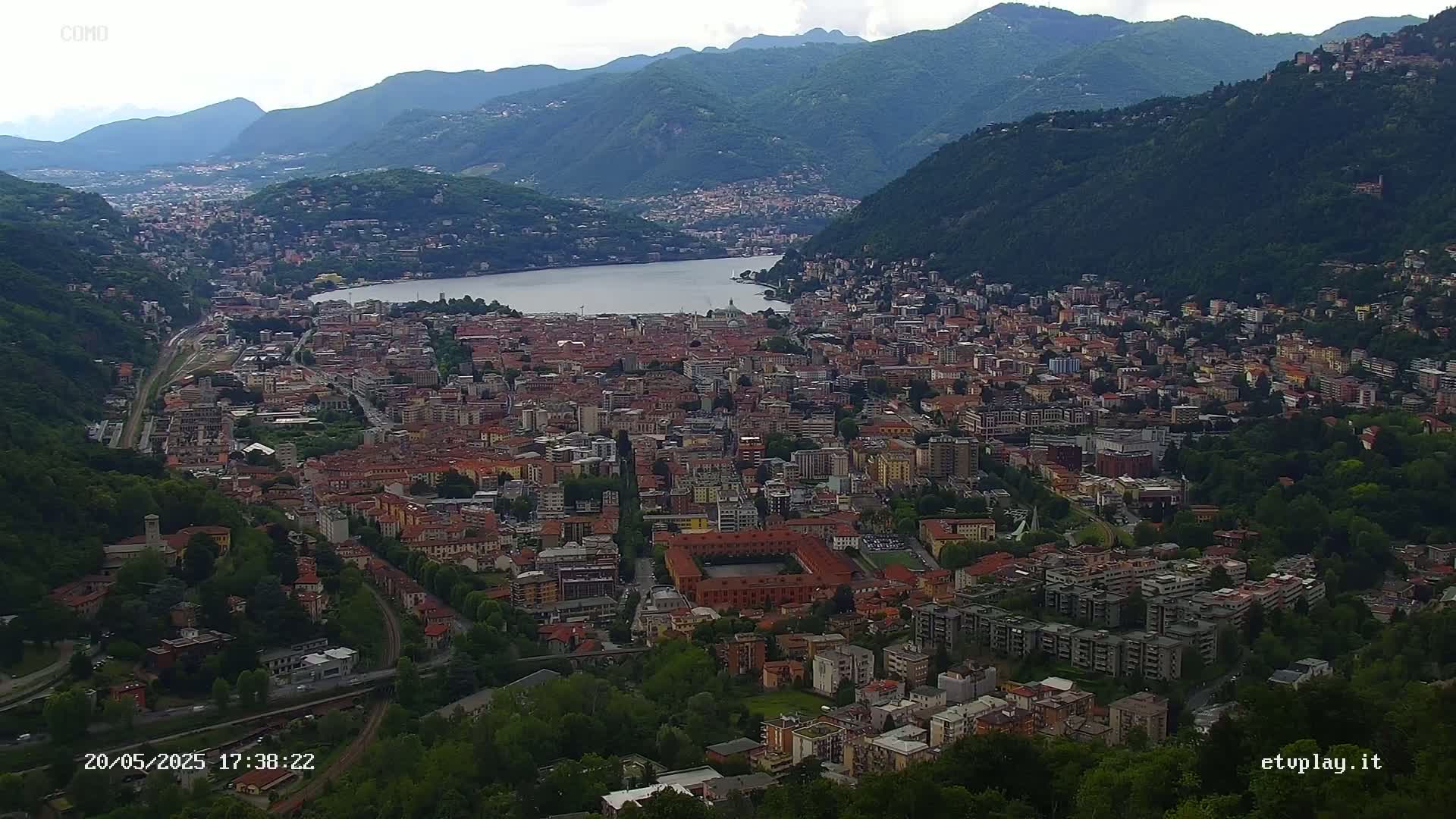 An expansive view of a city nestled between mountains and a lake under an overcast sky.