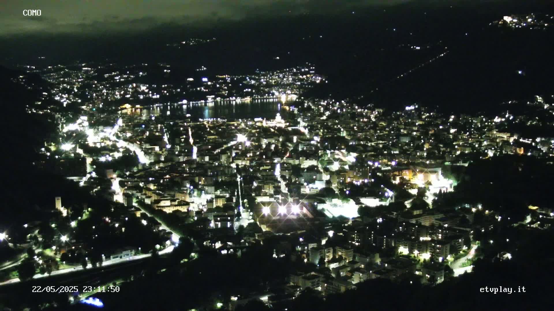 A nighttime, high-angle view of a city illuminated by lights, situated near a body of water under a mostly clear sky.