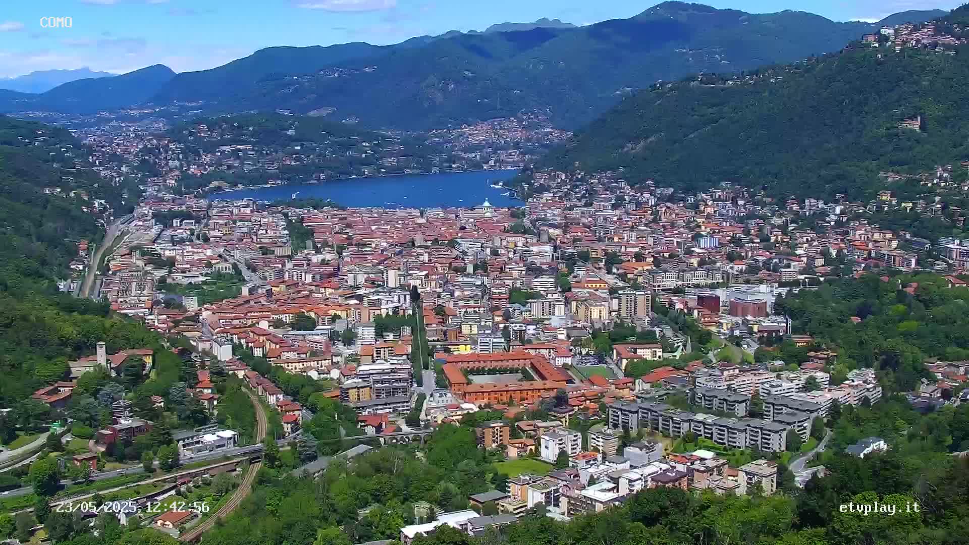 A sprawling city nestled in a valley between mountains, overlooking a calm lake under a clear sky.