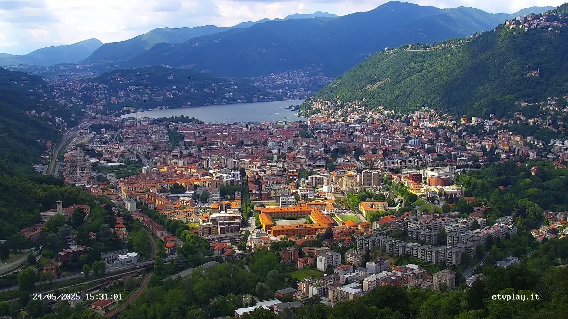 A sprawling city nestled between mountains and a lake under a partly cloudy sky.
