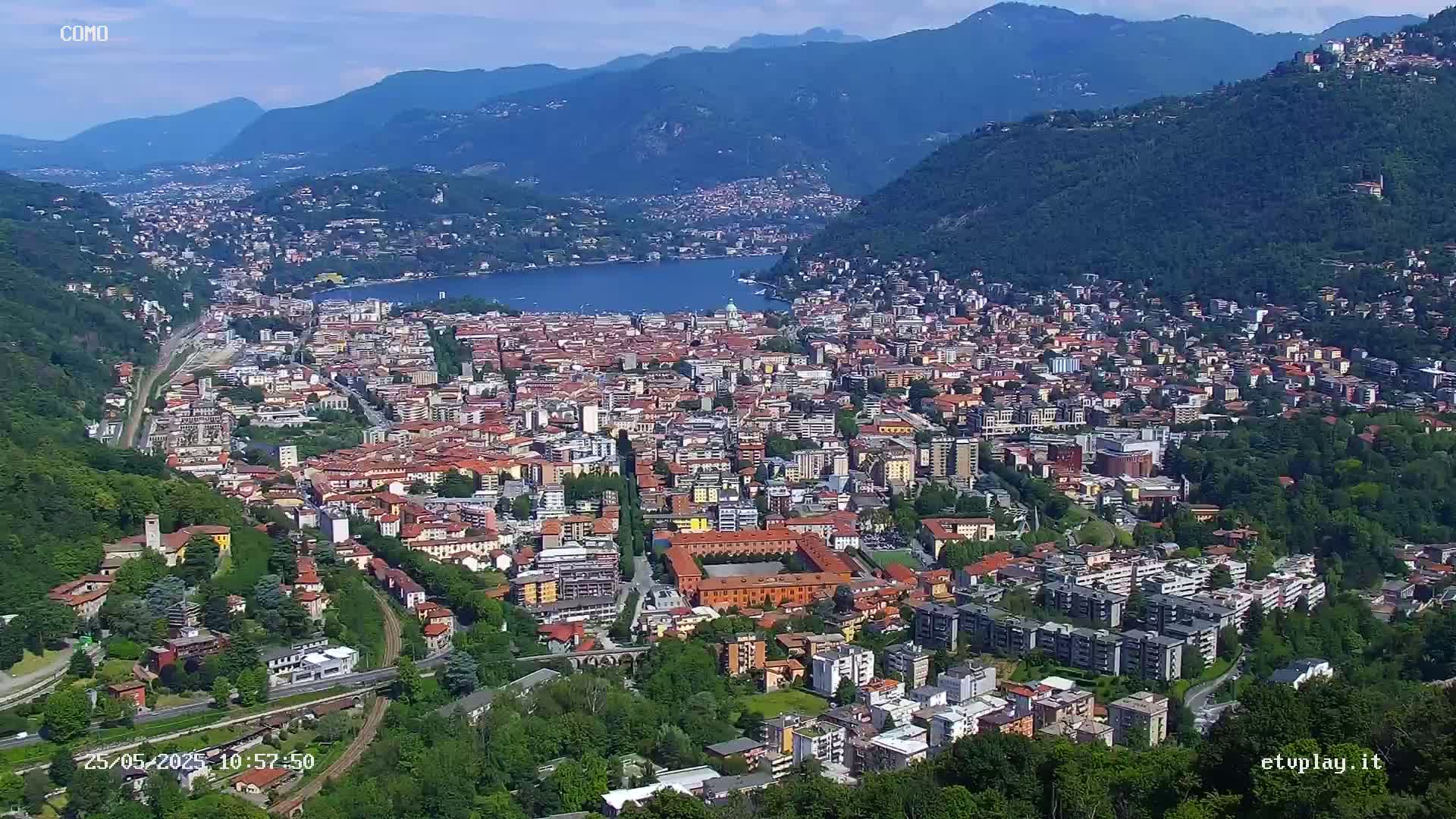 A sprawling city nestled in a valley between mountains, with a large lake visible in the distance under a clear sky.