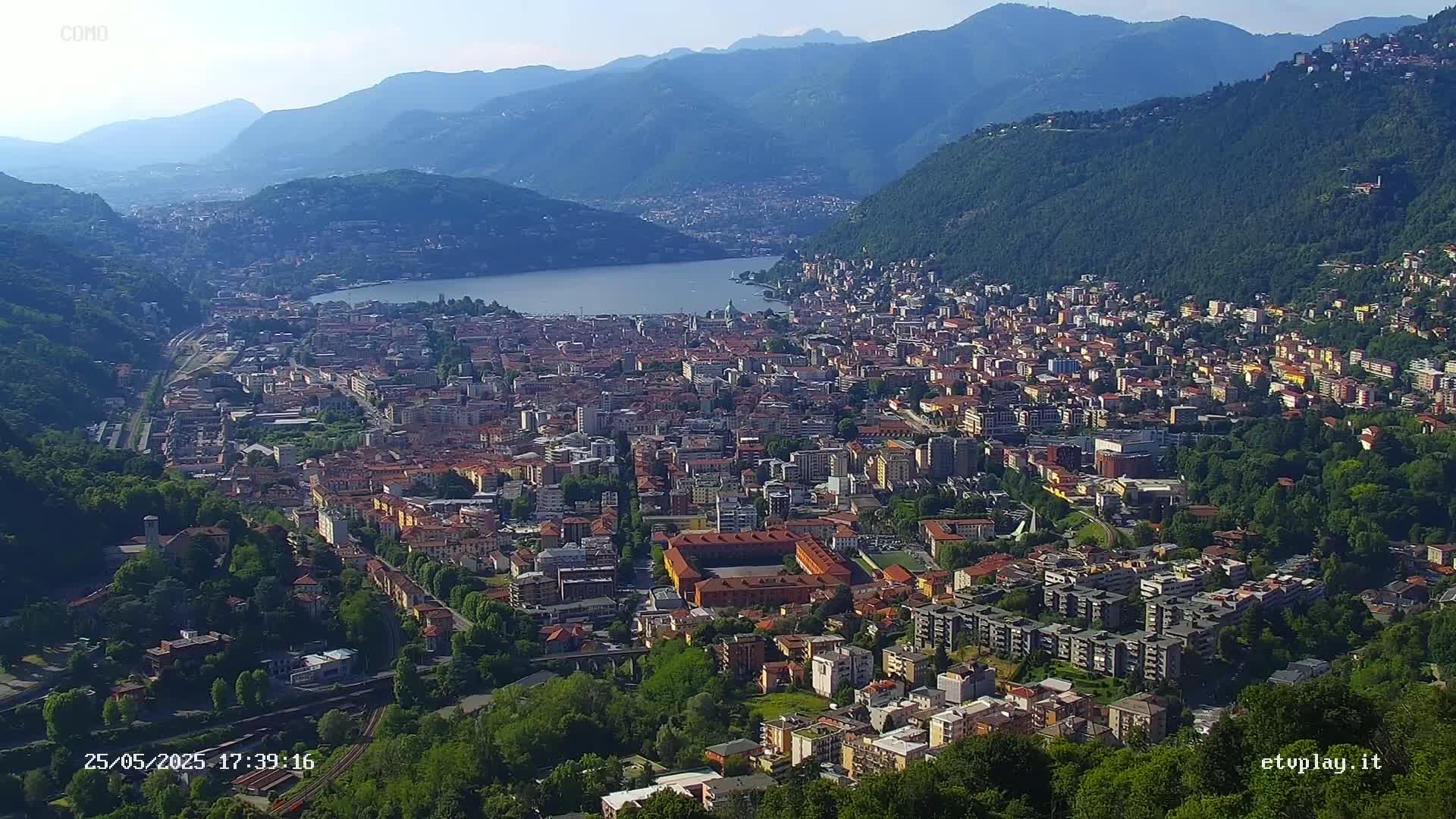 A sprawling city nestled in a valley beside a lake, surrounded by mountains under a clear sky.