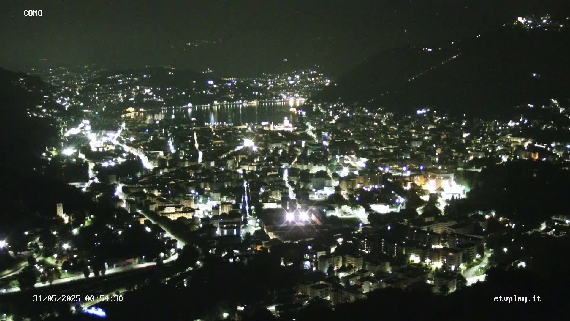 A nighttime, aerial view of a city illuminated by lights, situated beside a body of water under a clear sky.