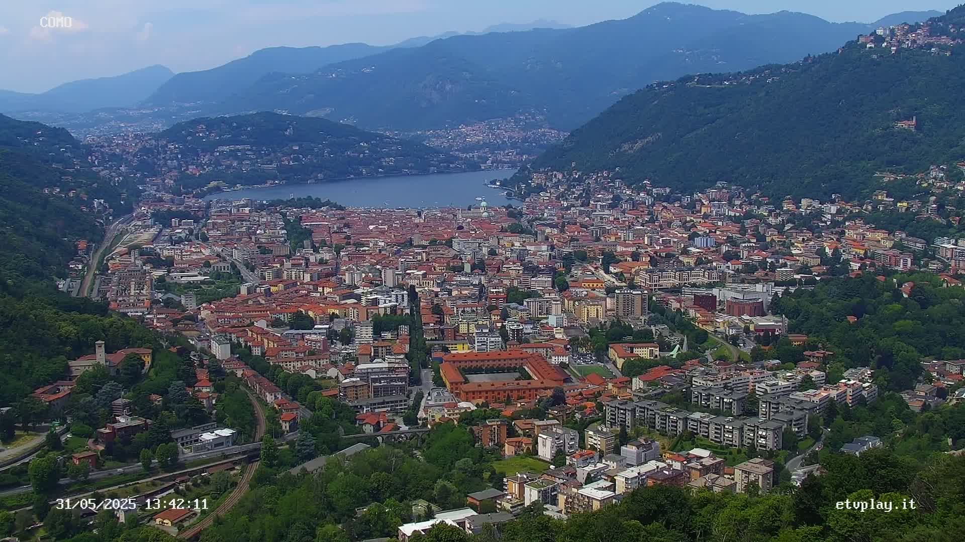 A sprawling city nestled in a valley between mountains, next to a lake under a mostly clear sky.