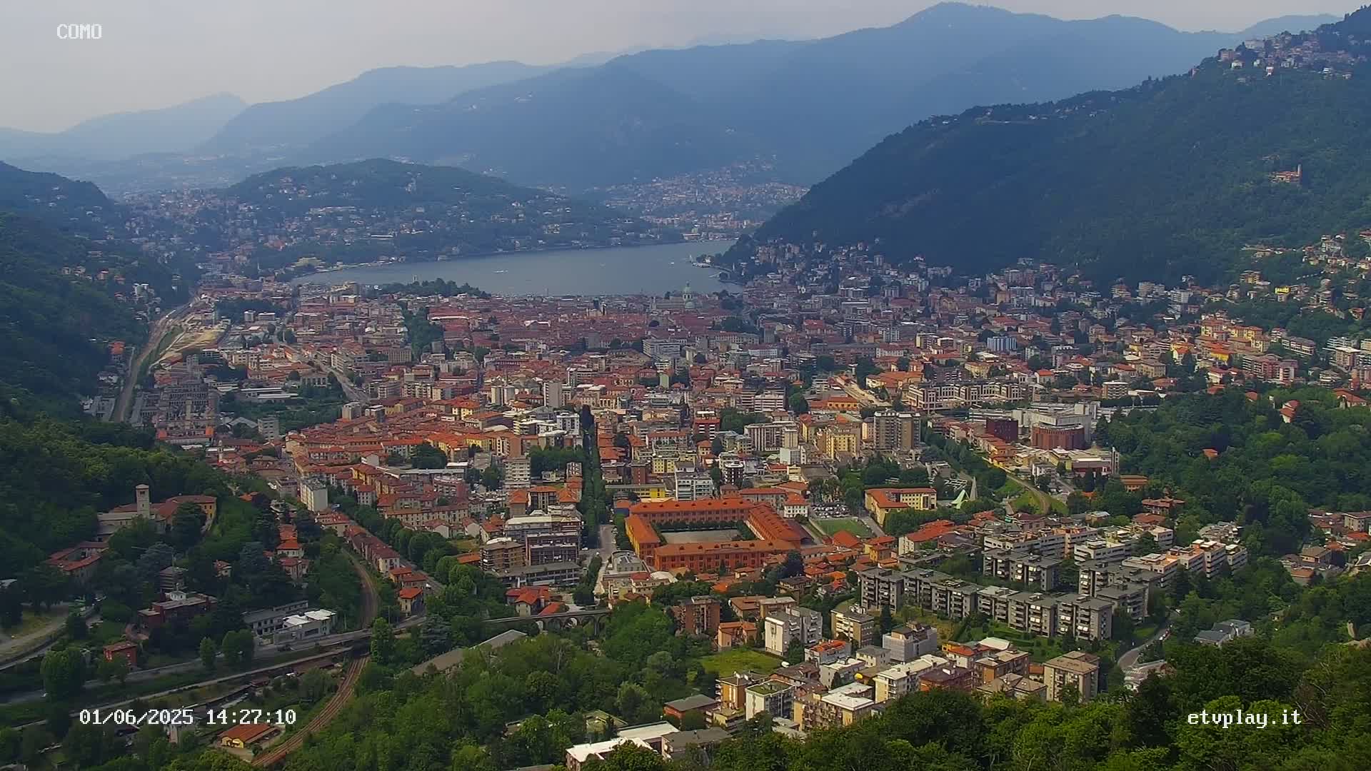A sprawling city nestled between mountains and a lake on a hazy day.