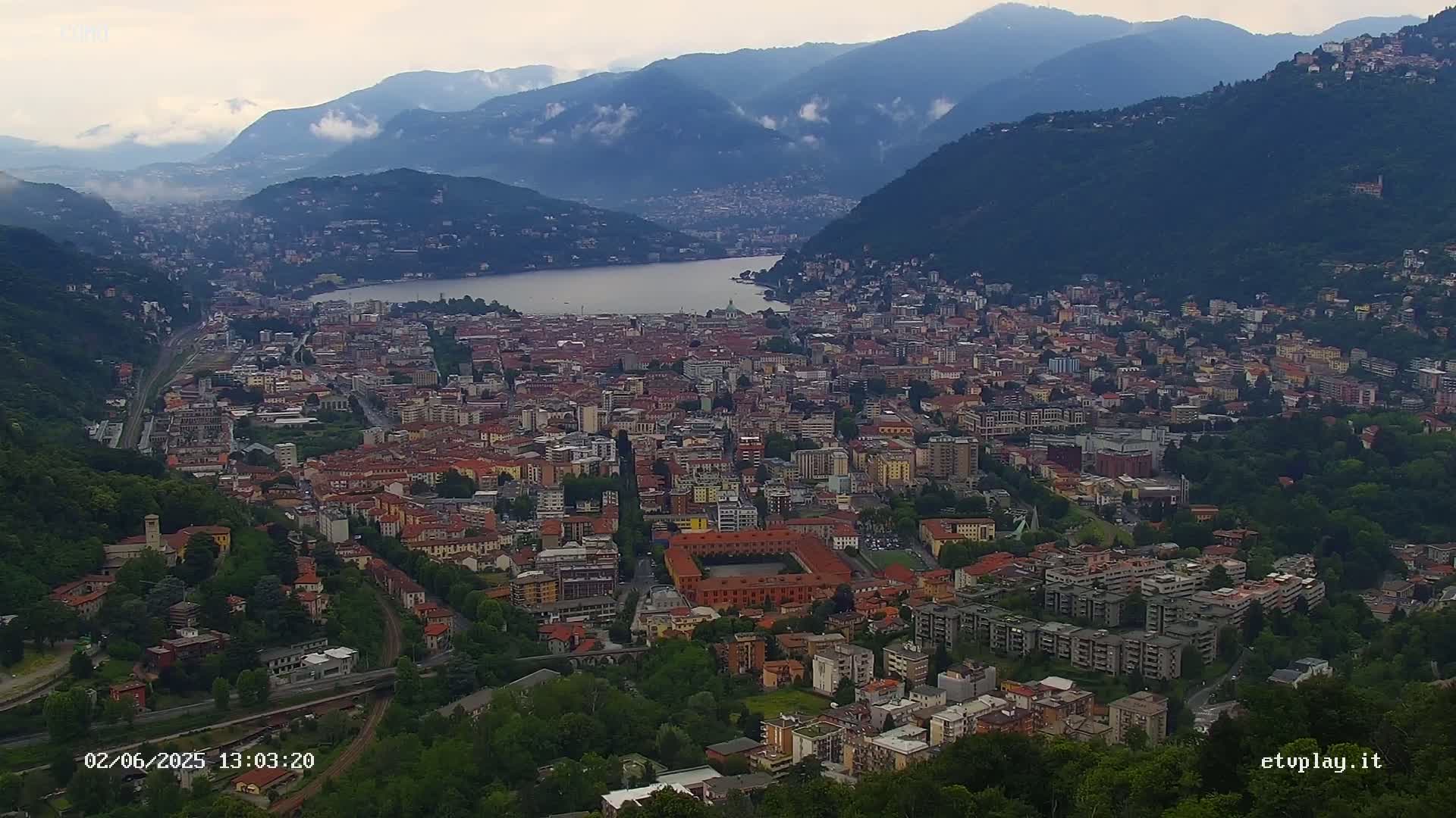 An expansive city nestled between mountains and a lake, partially shrouded in mist.