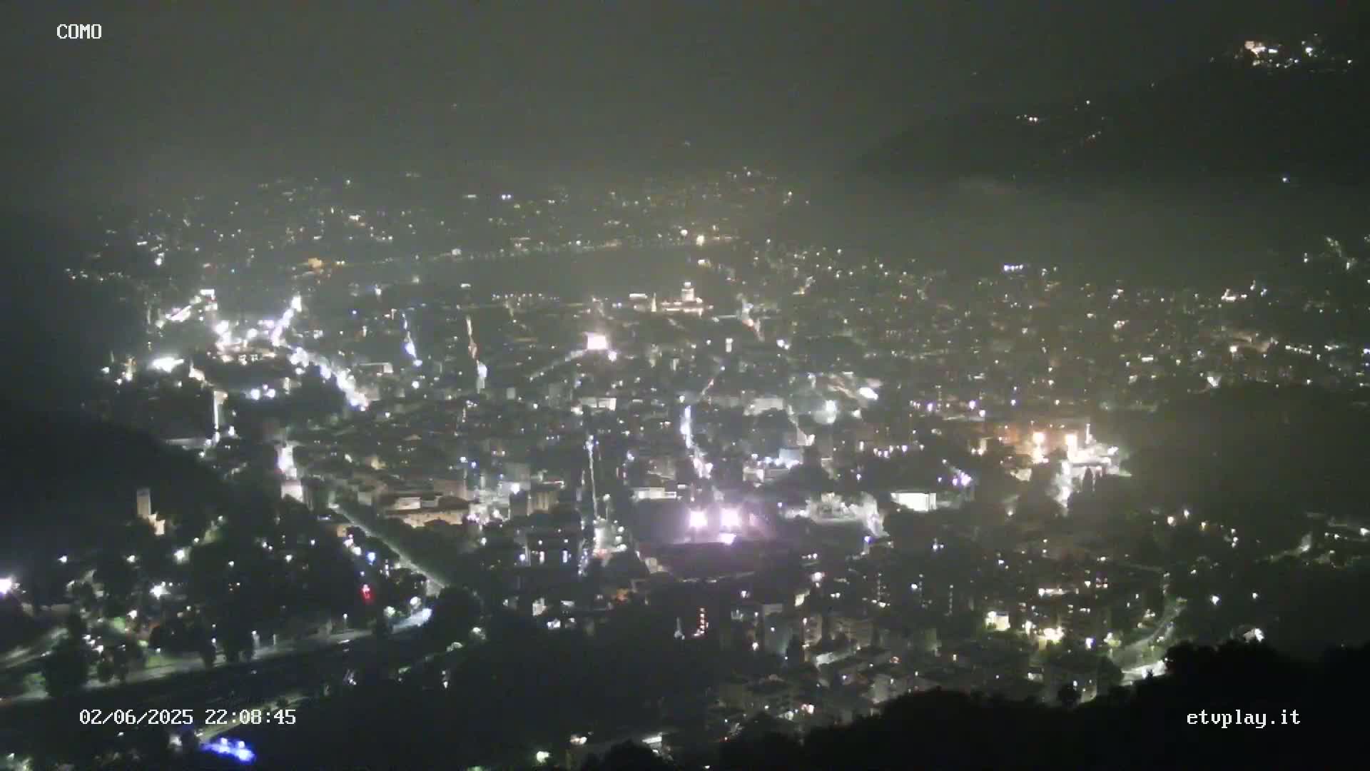 A nighttime, high-angle view of a city illuminated by streetlights and other lights, under a hazy sky.