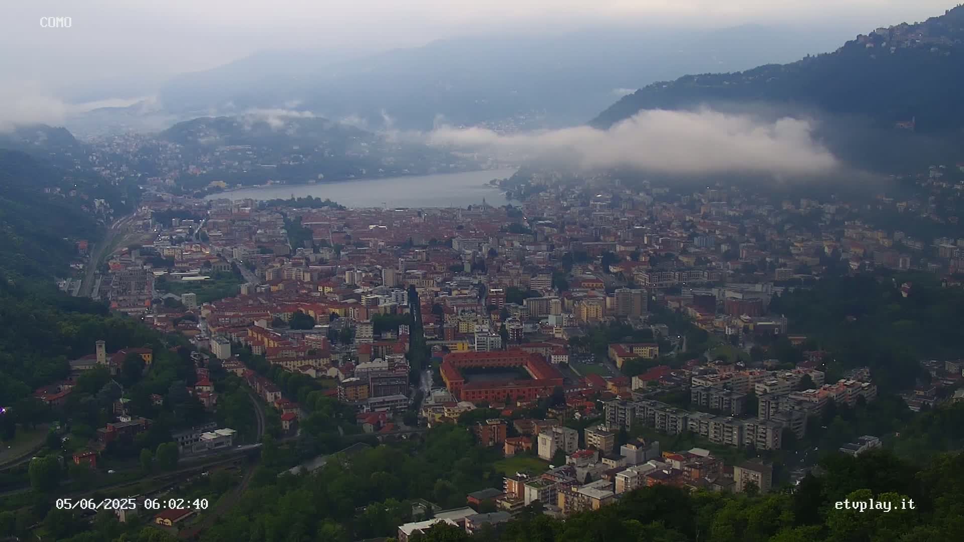 A sprawling city nestled between a lake and mountains, partially shrouded in fog.