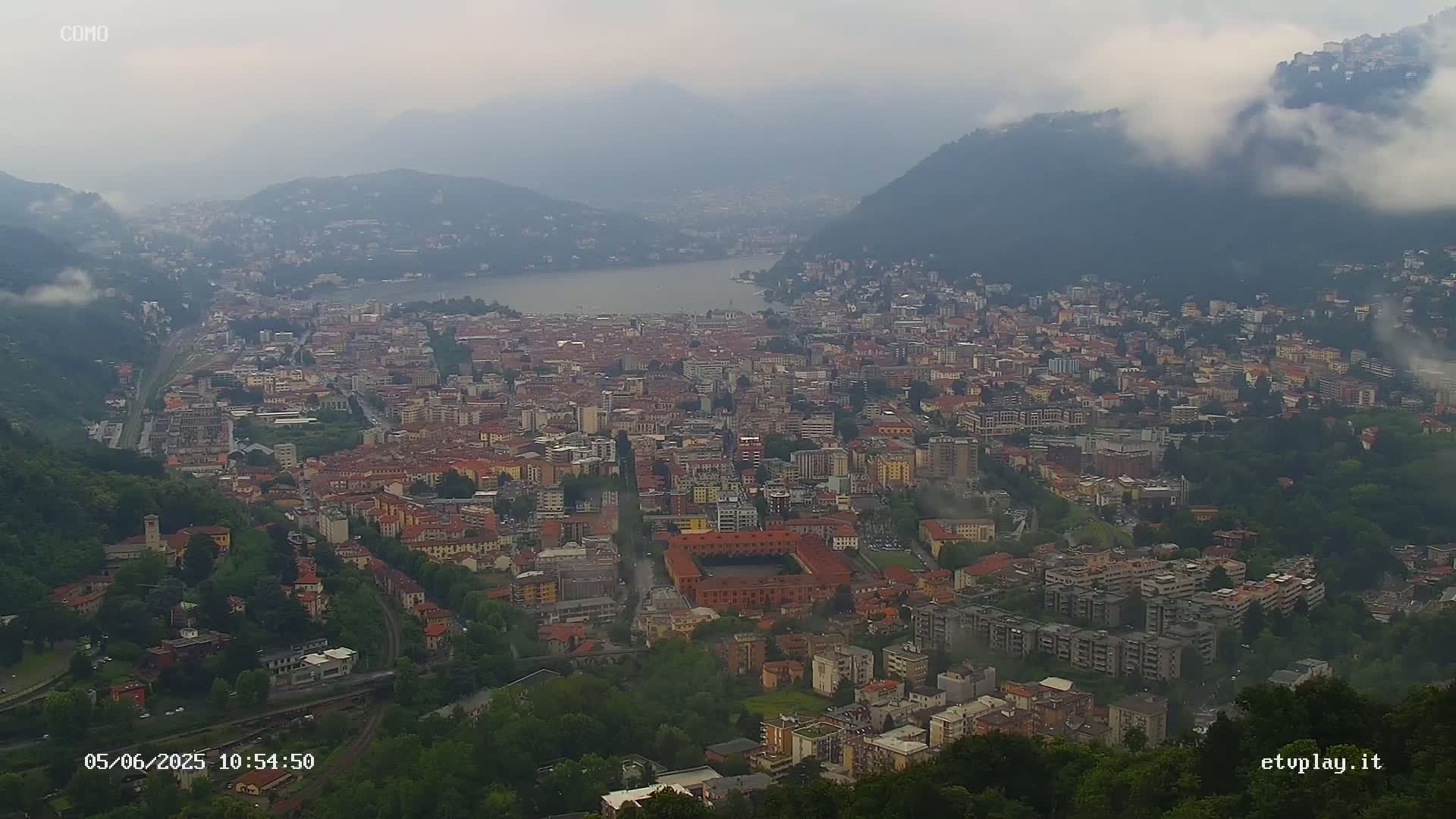 A sprawling city nestled between hills and a lake, partially obscured by fog.