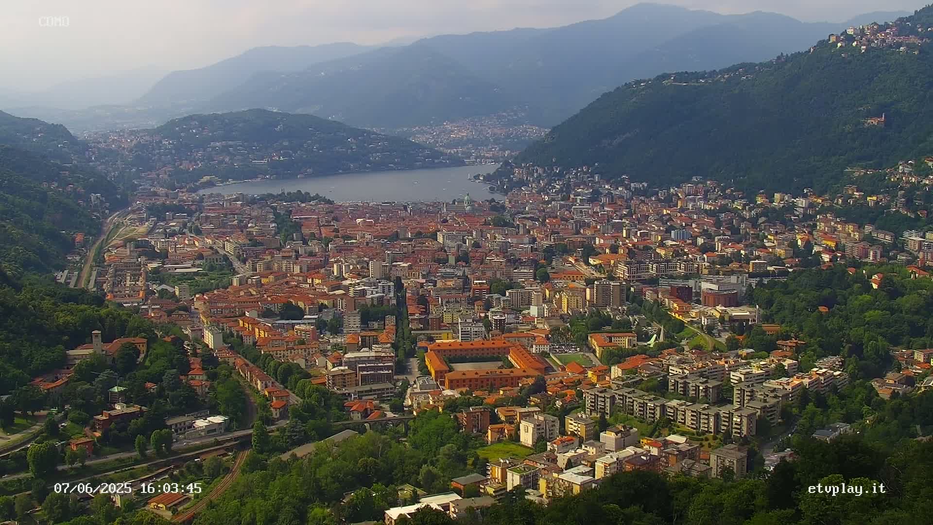 An expansive view of a city nestled between hills and a lake on a hazy day.