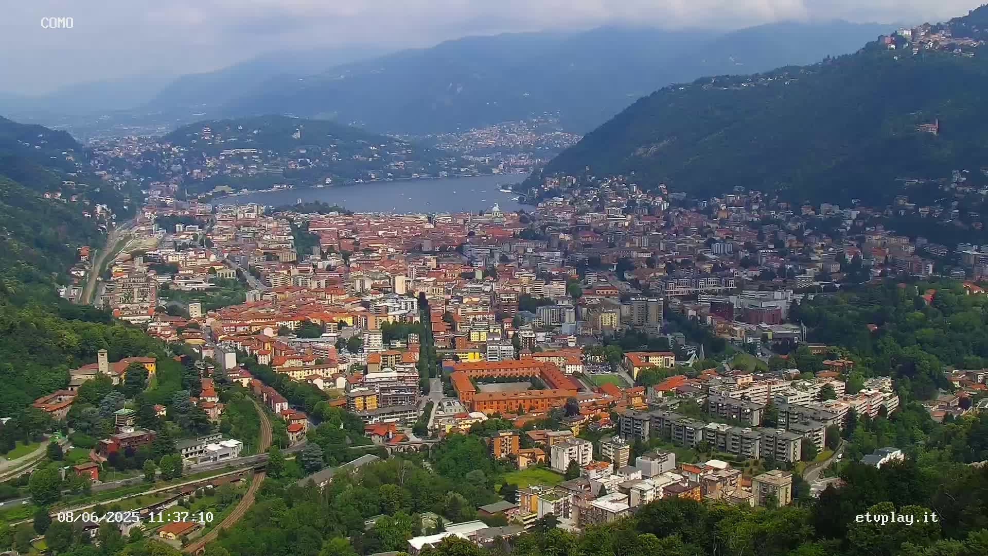 A sprawling city nestled between mountains and a lake under partly cloudy skies.