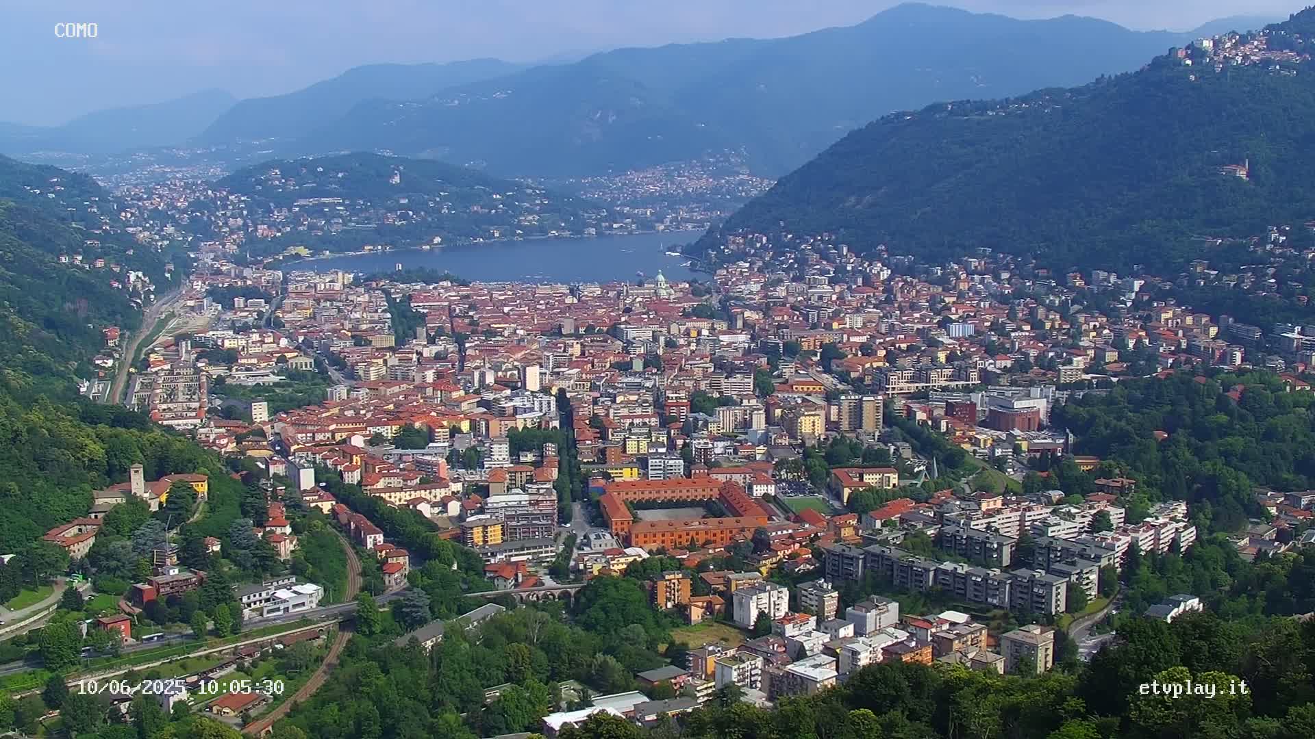 An aerial view of a city nestled between mountains and a lake on a clear day.