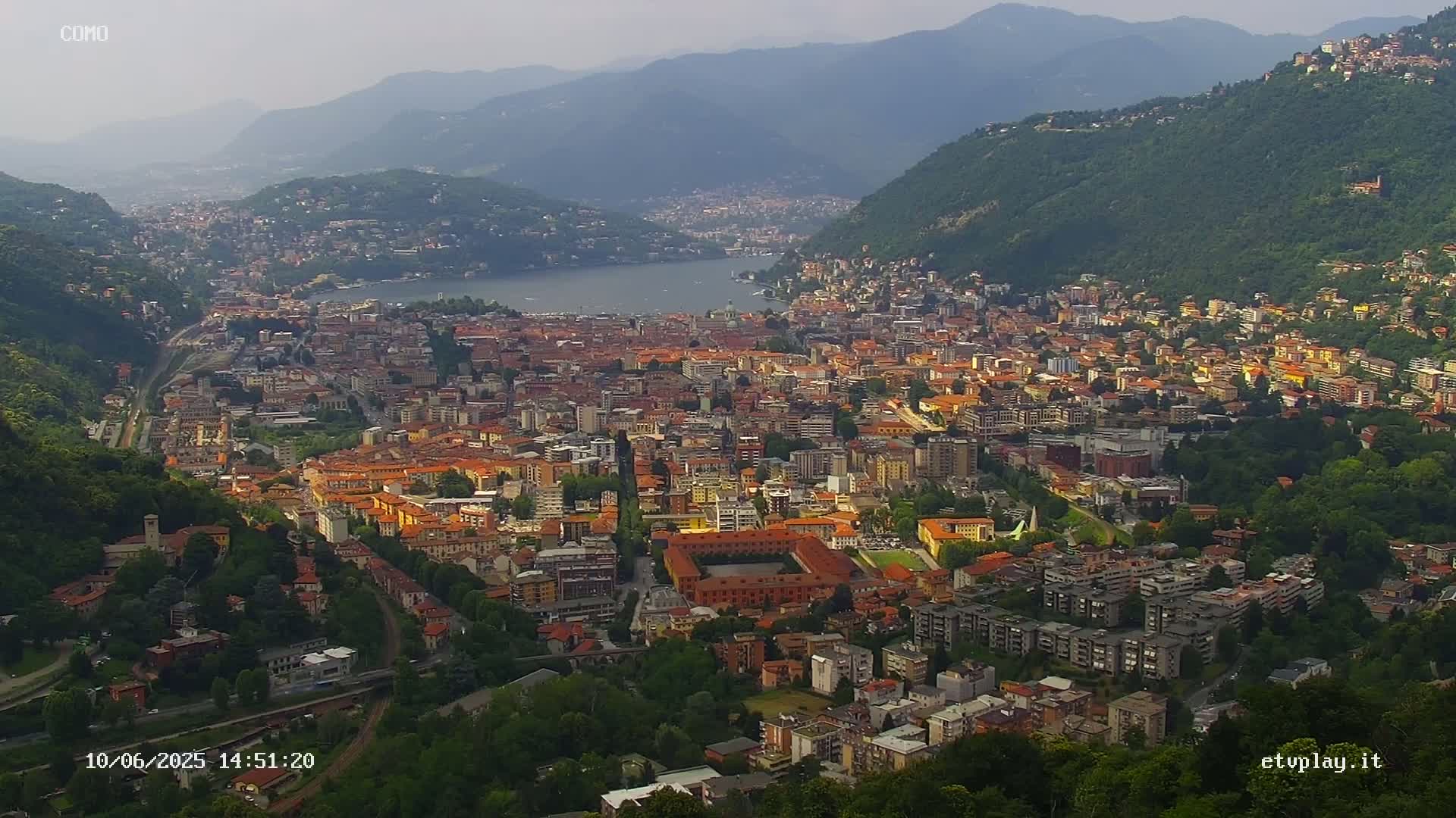 A sprawling city nestled between mountains and a lake under a hazy sky.
