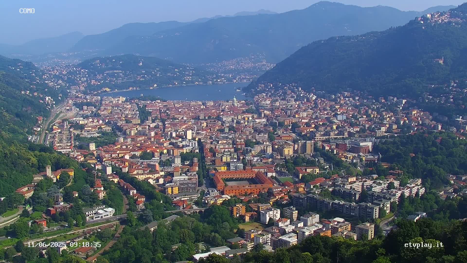 A sprawling city nestled between mountains and a lake on a clear, sunny day.