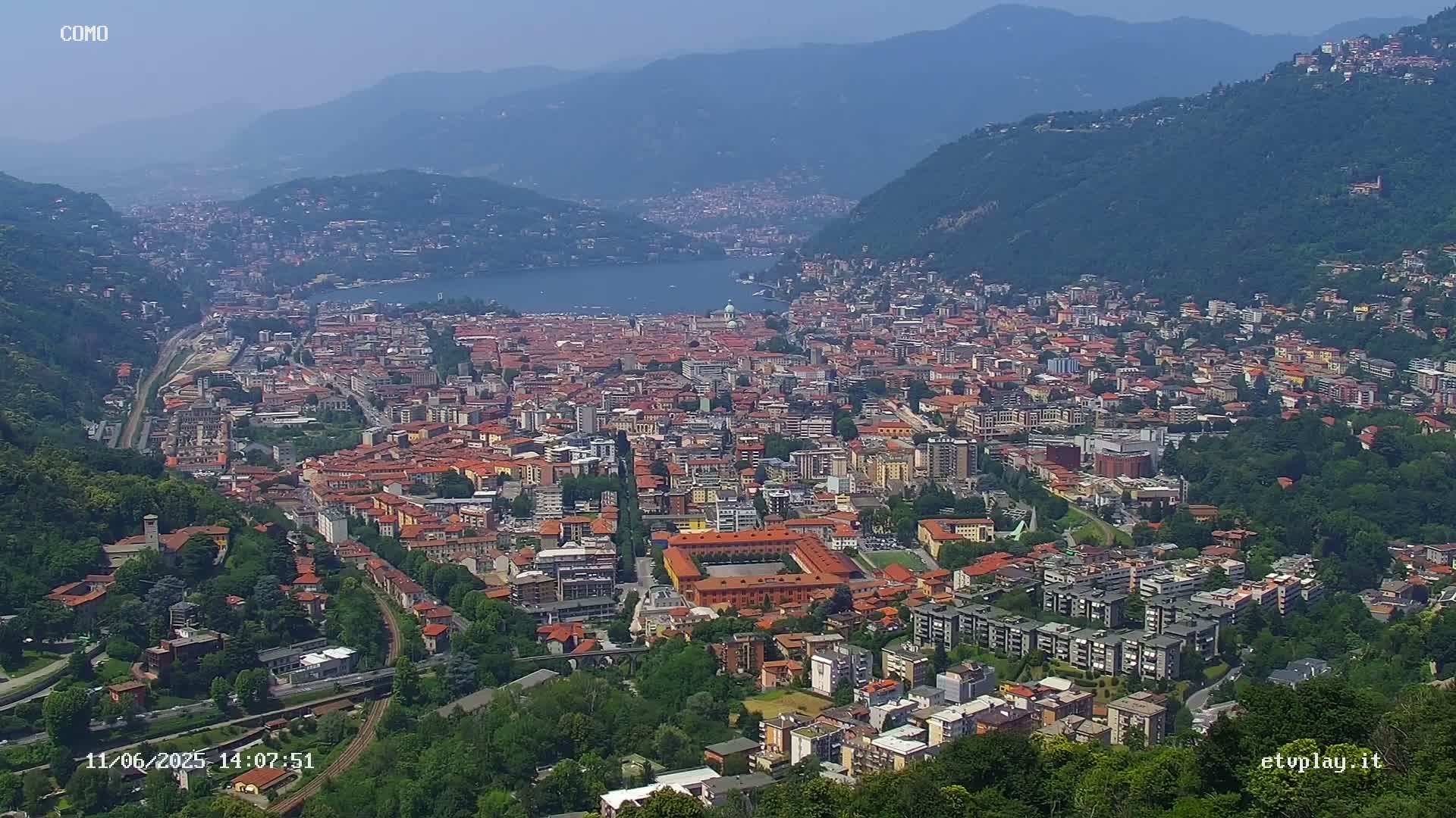 A sprawling city nestled in a valley between mountains, overlooking a lake on a clear, sunny day.