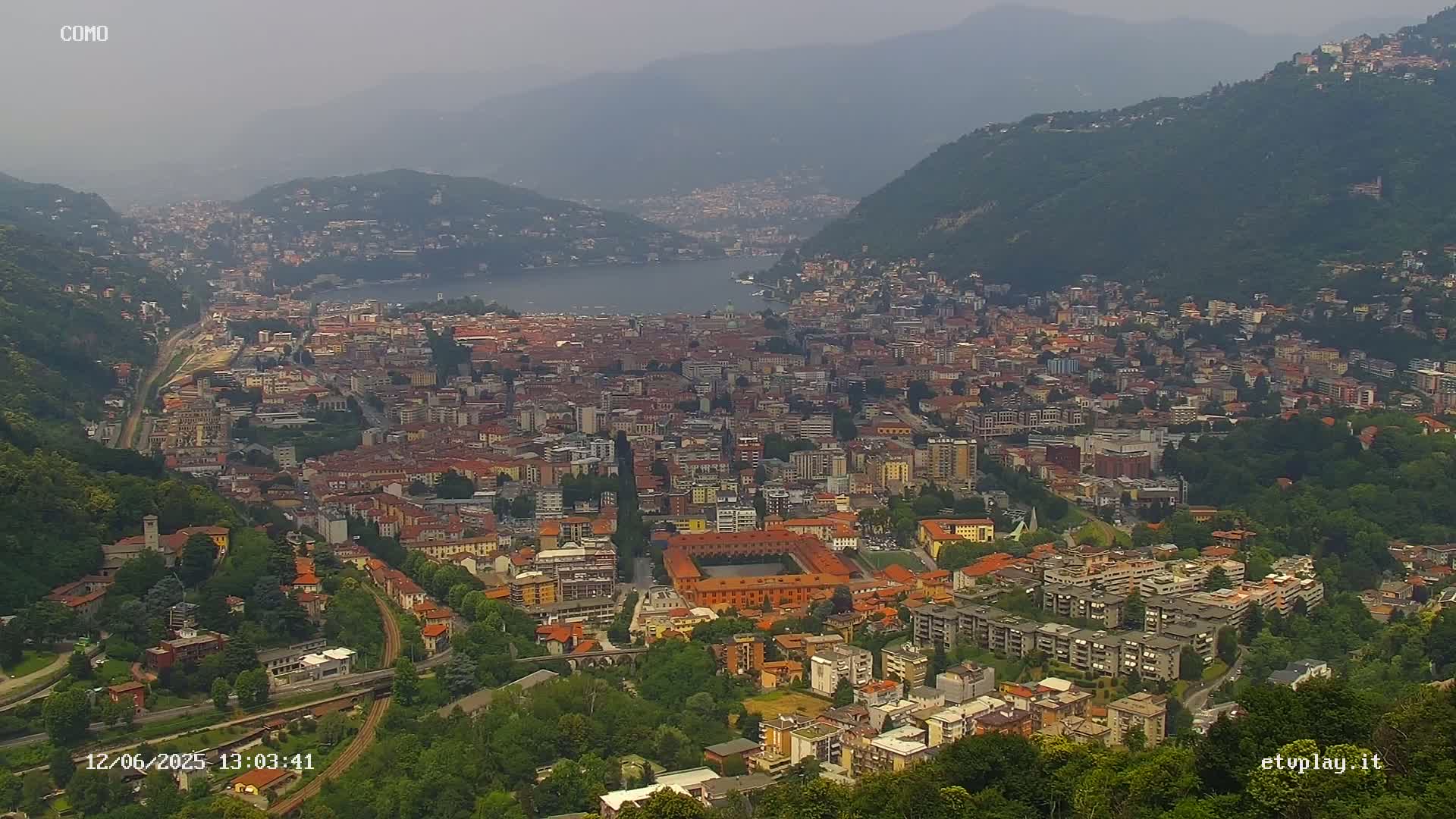 A hazy view overlooking a city nestled between hills and a lake.
