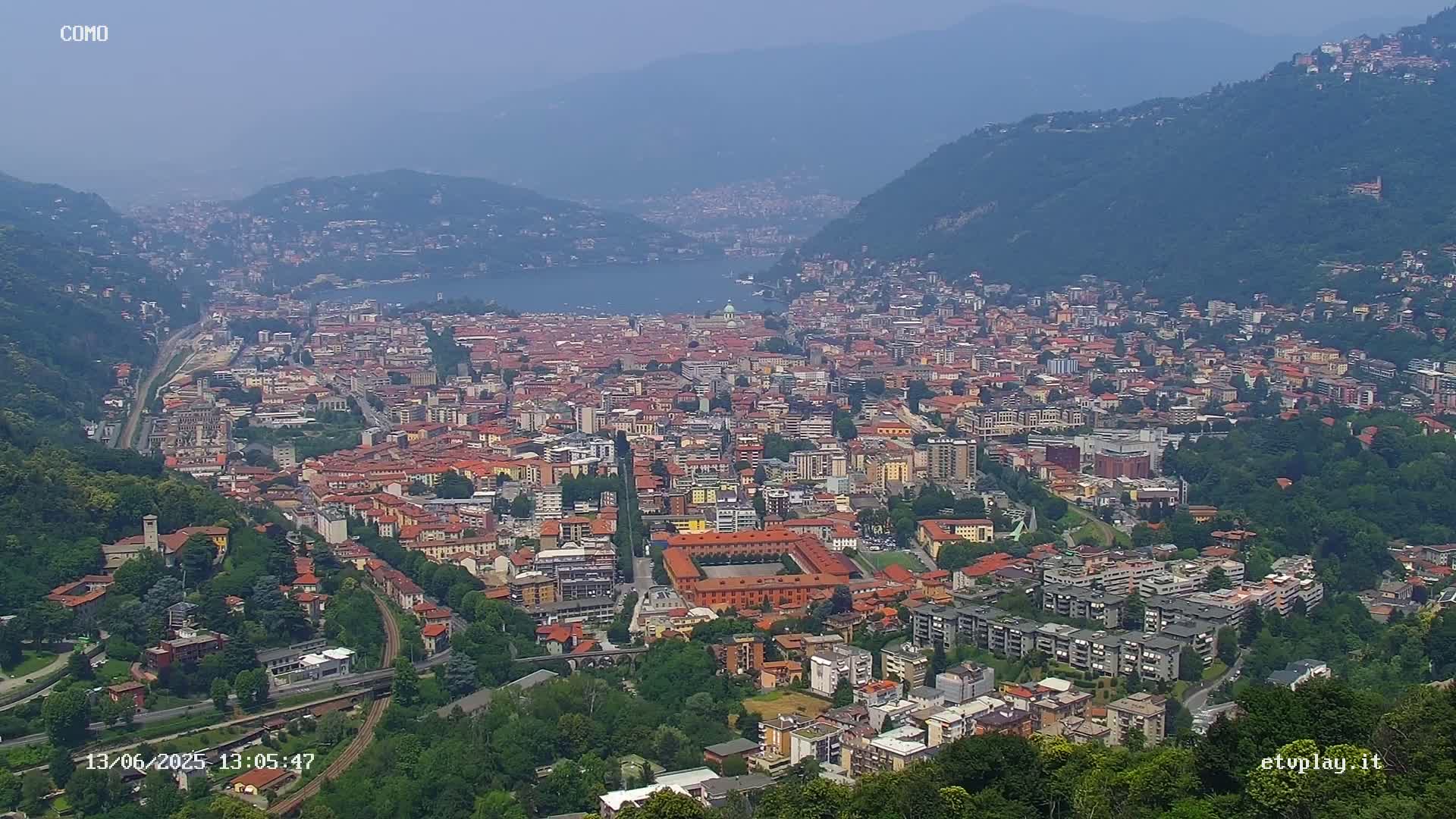 A sprawling city nestled between mountains and a lake on a hazy day.
