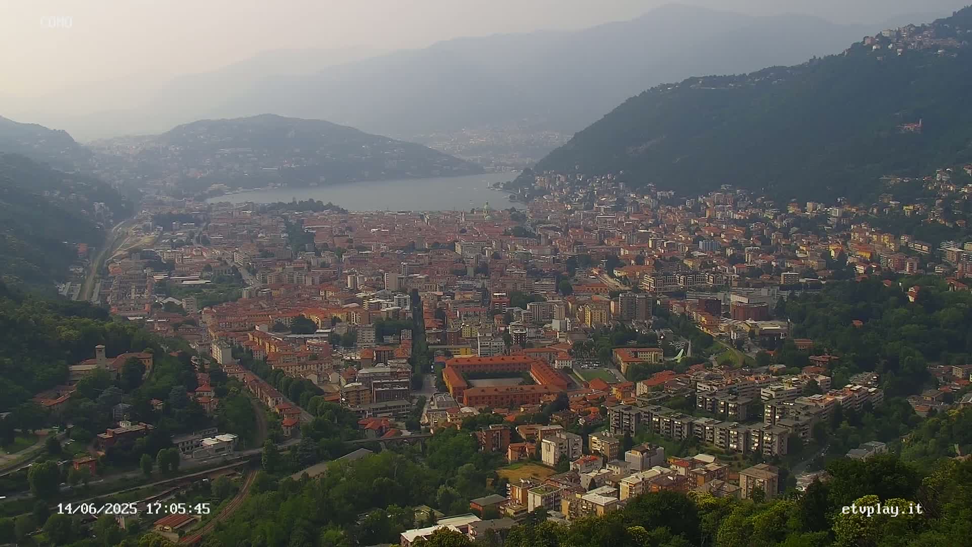 A hazy, high-angle view of a large city nestled between mountains and a lake.