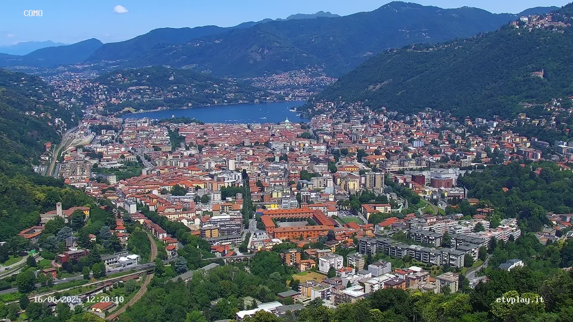 A sprawling city nestled in a valley between mountains, next to a lake under a clear blue sky.