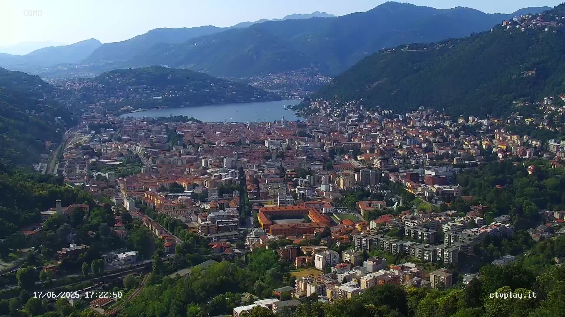 A sprawling city nestled between mountains and a lake on a clear, sunny day.