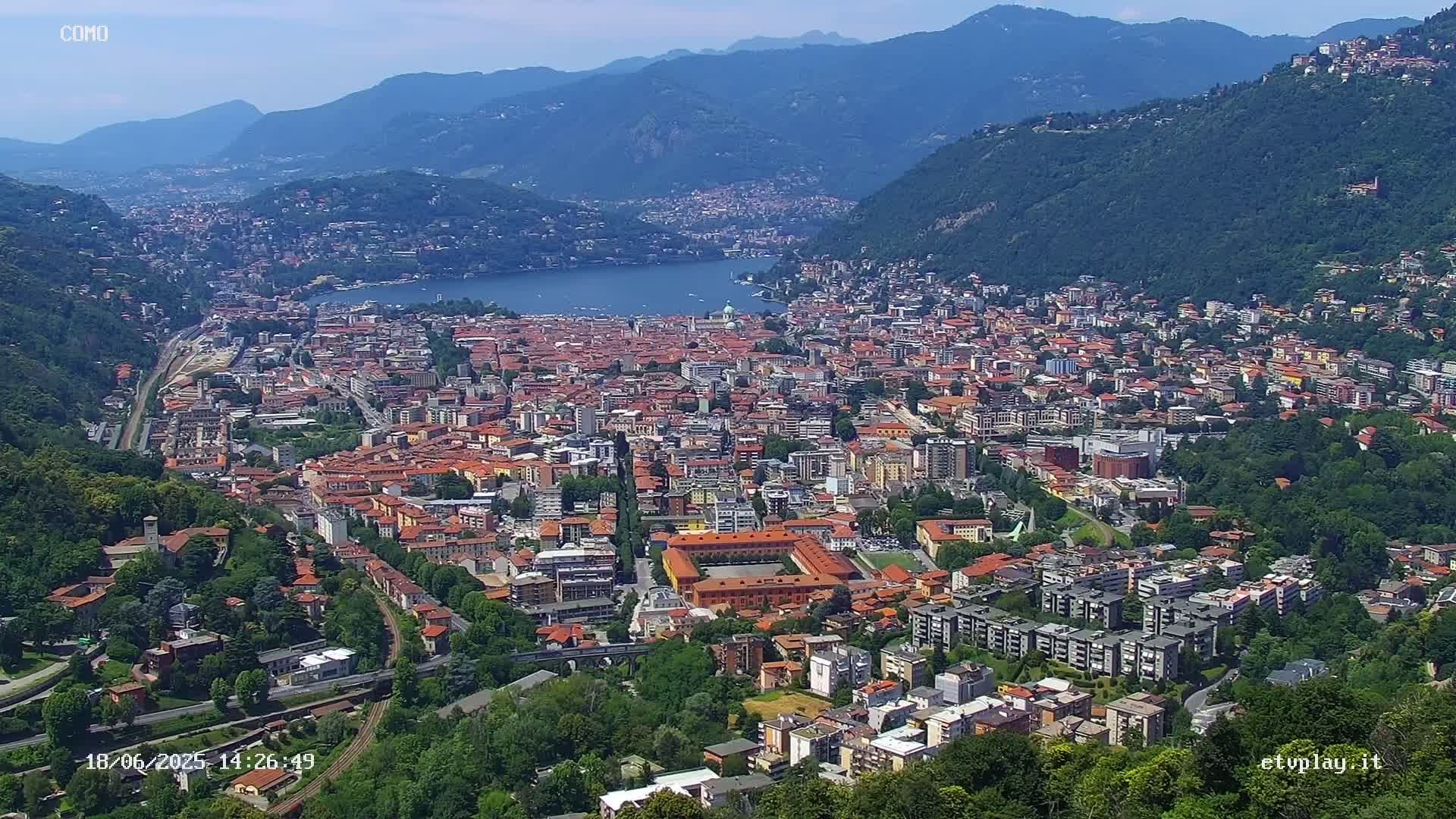 An aerial view of a city nestled in a valley alongside a lake, under a mostly clear sky.
