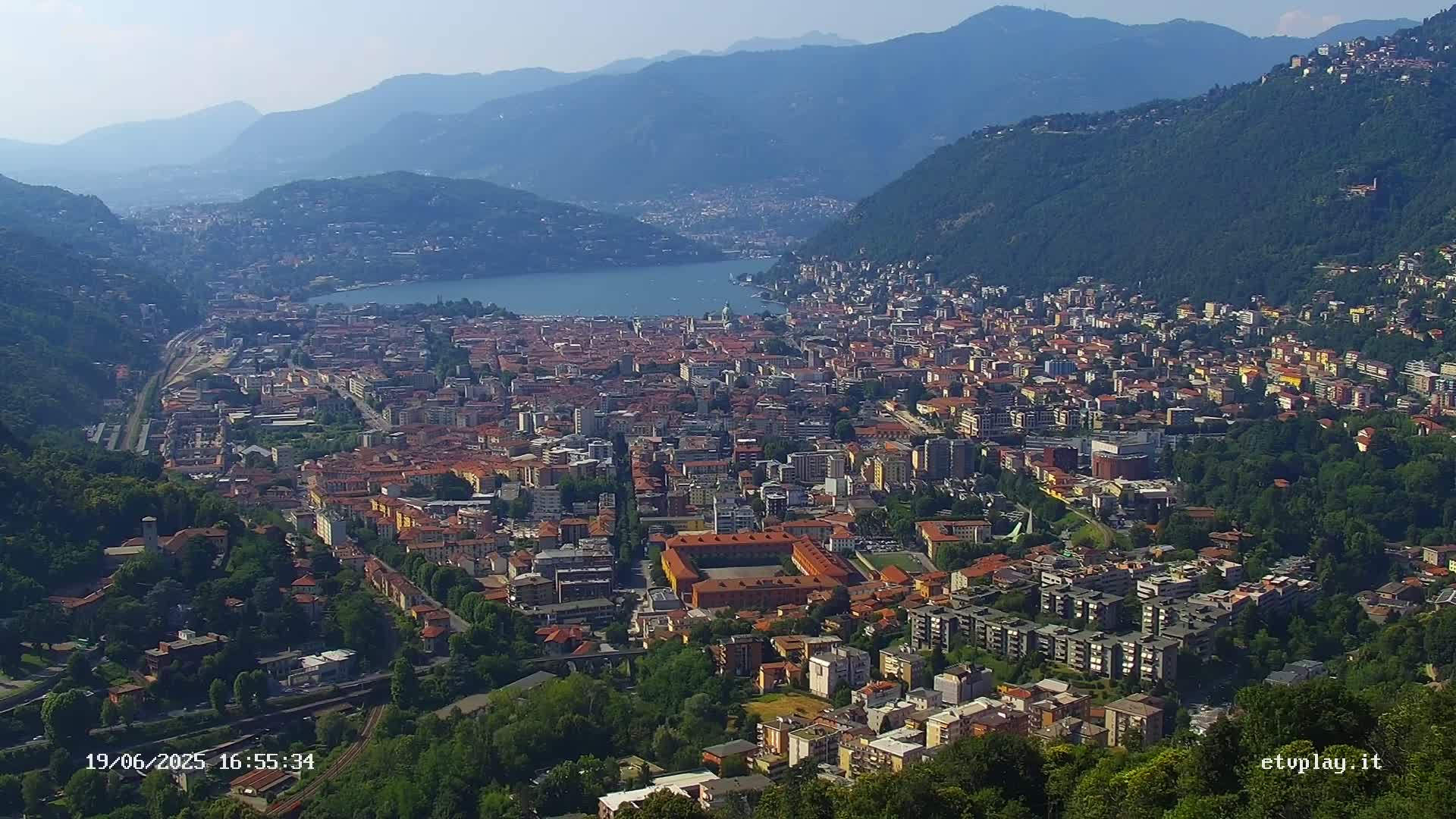 A sprawling city nestled in a valley between mountains, overlooking a lake under a clear sky.