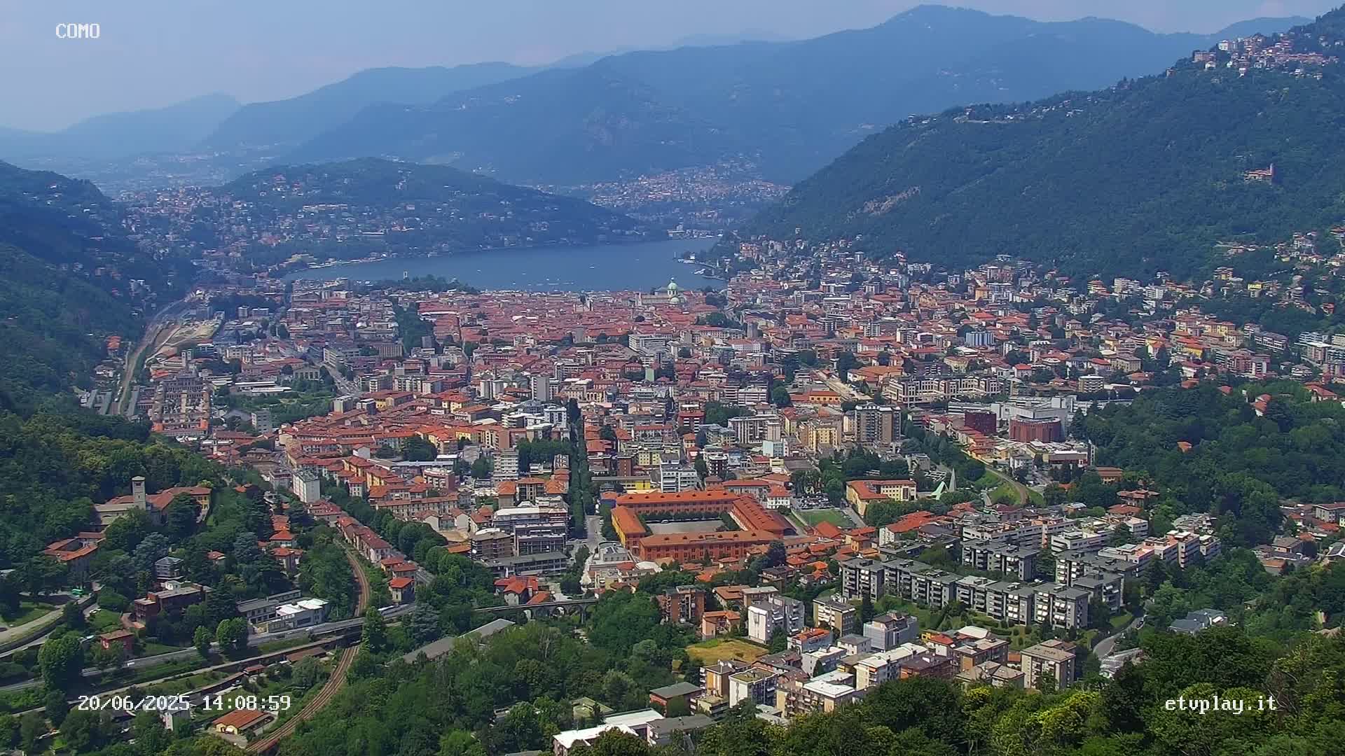 A sprawling city nestled between mountains and a lake on a clear, sunny day.