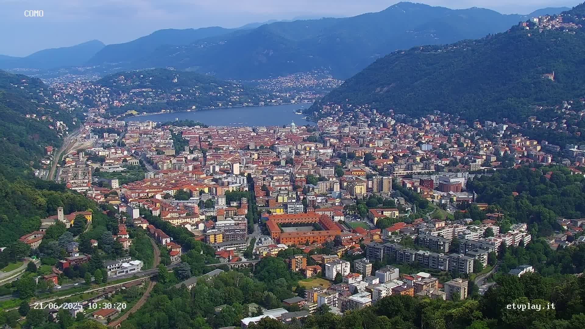 A sprawling city nestled in a valley between mountains, overlooking a calm lake under a clear sky.