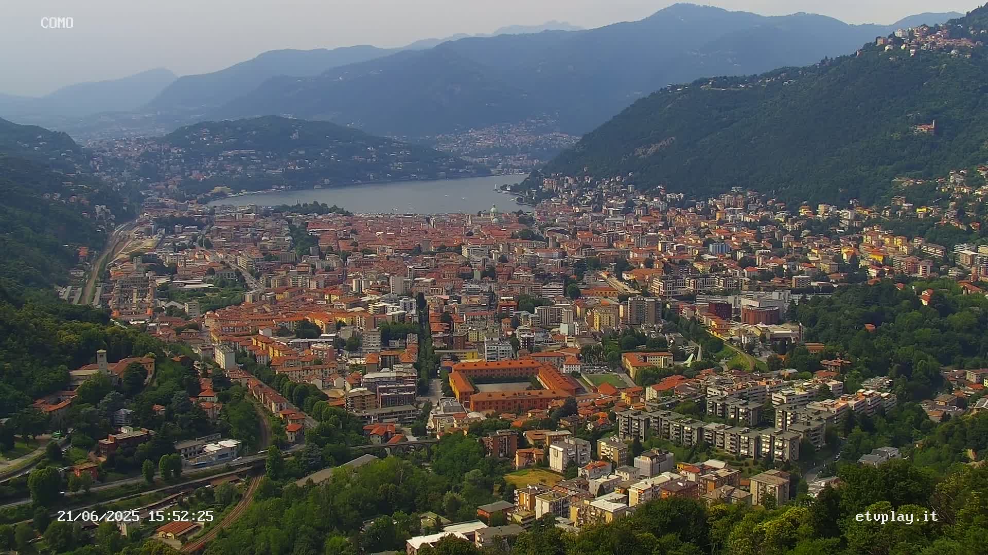 An expansive view of a city nestled between mountains and a lake on a hazy day.