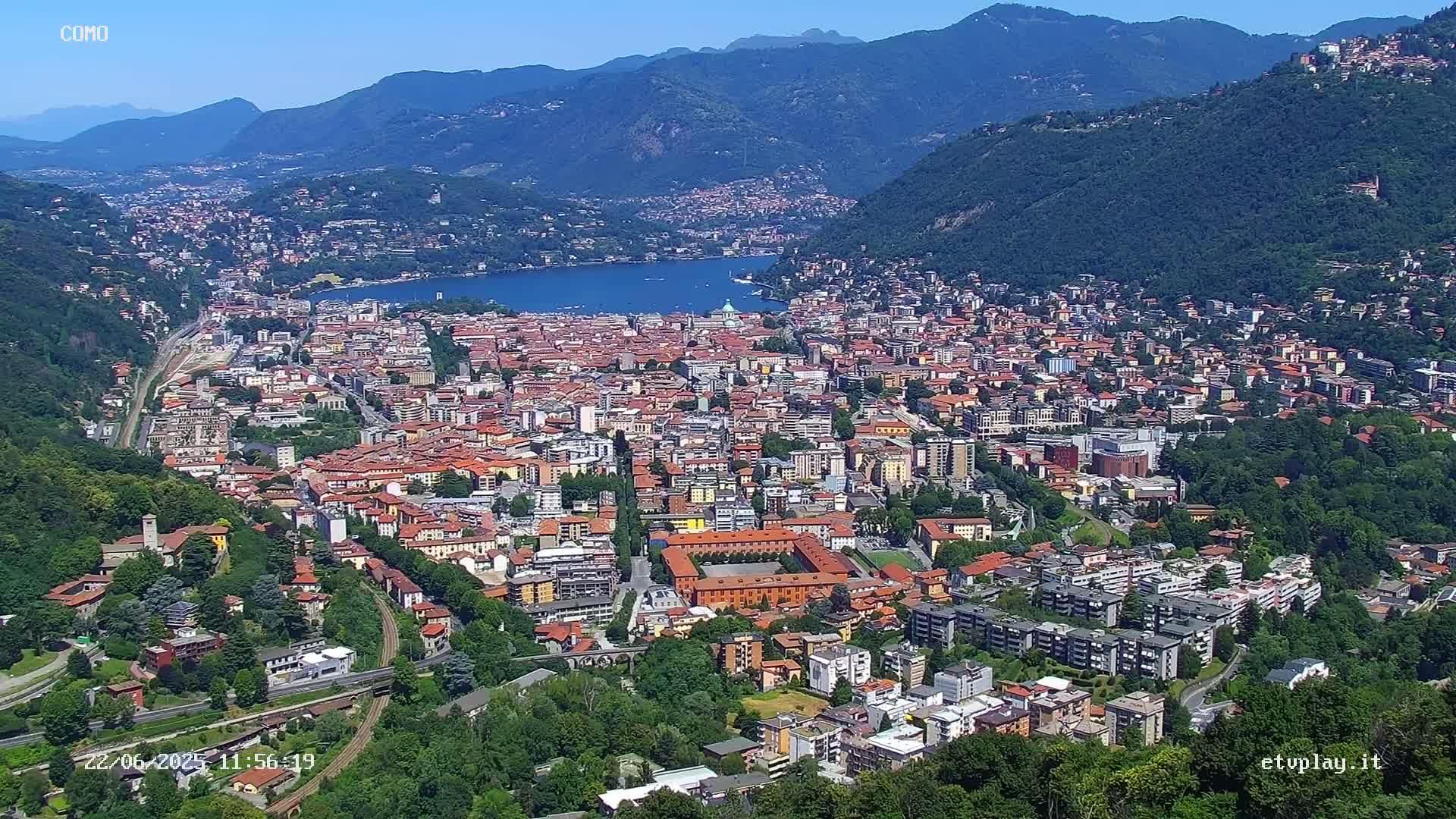 A sprawling city nestled in a valley between mountains, overlooking a calm lake under a clear blue sky.