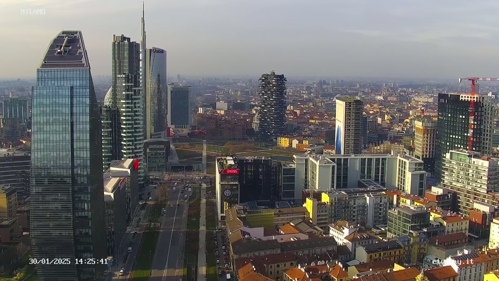 An aerial view of a city's skyline, featuring numerous skyscrapers and high-rise buildings under a hazy, sunny sky.