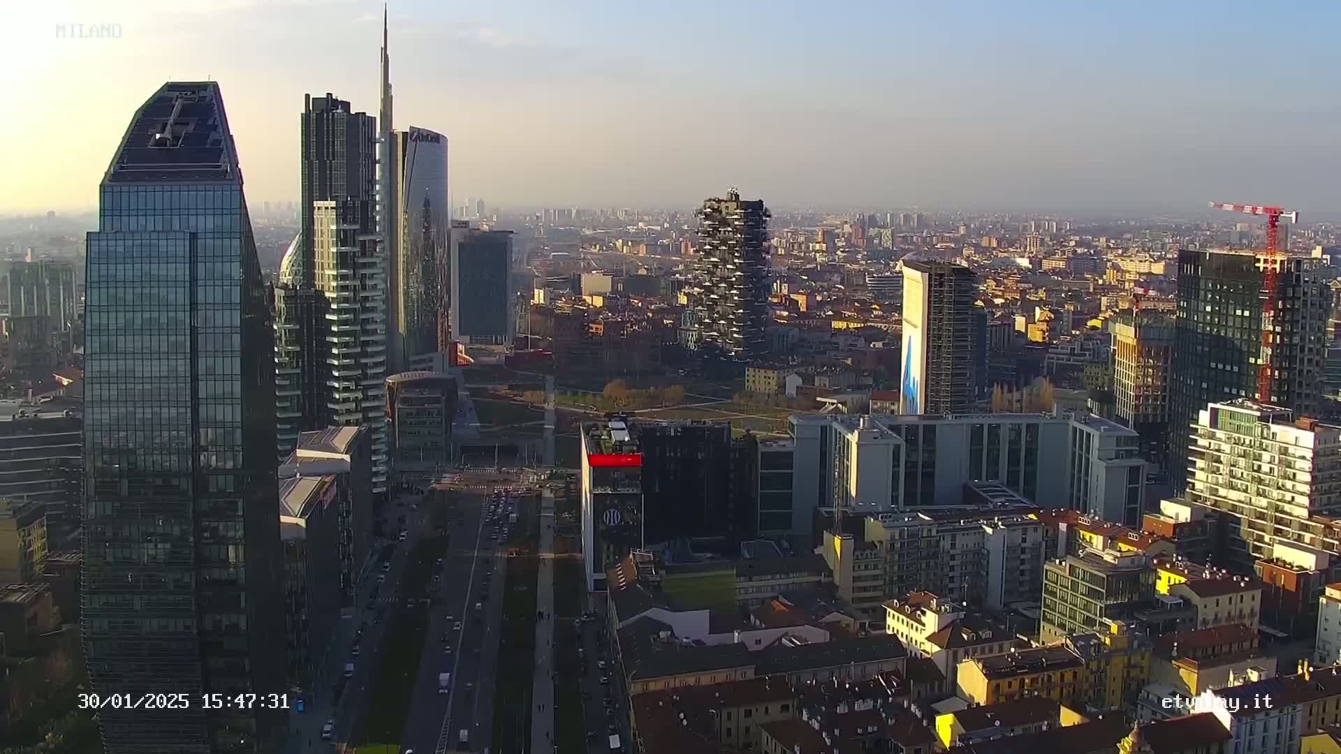 An aerial view of a dense cityscape of skyscrapers and residential buildings under a hazy, sunny sky.