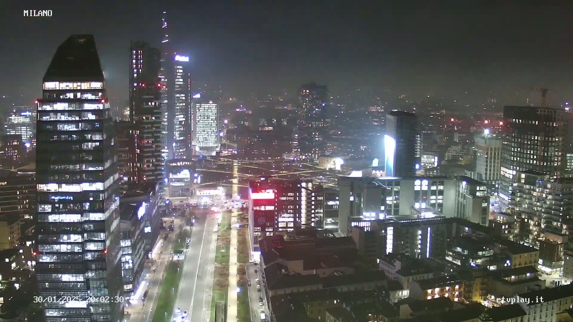 A nighttime aerial view of a city skyline with numerous illuminated skyscrapers under hazy conditions.