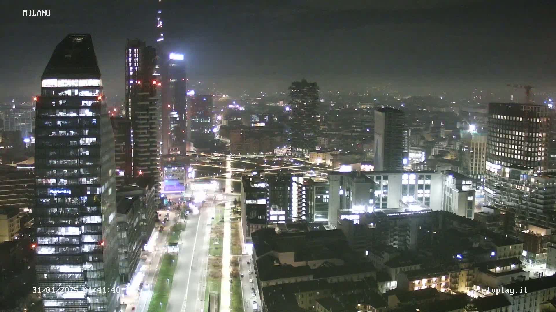 A nighttime aerial view of a city with numerous illuminated skyscrapers and buildings, under hazy or foggy conditions.