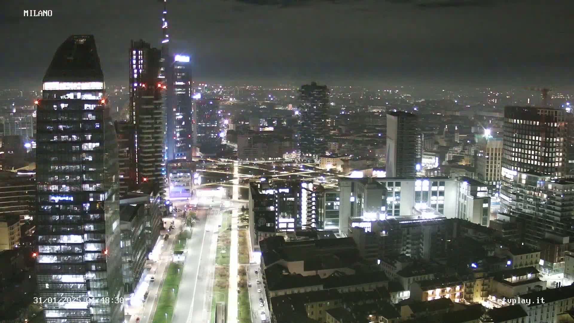 A nighttime aerial view of a city, showing numerous illuminated skyscrapers and buildings under a dark, clear sky.