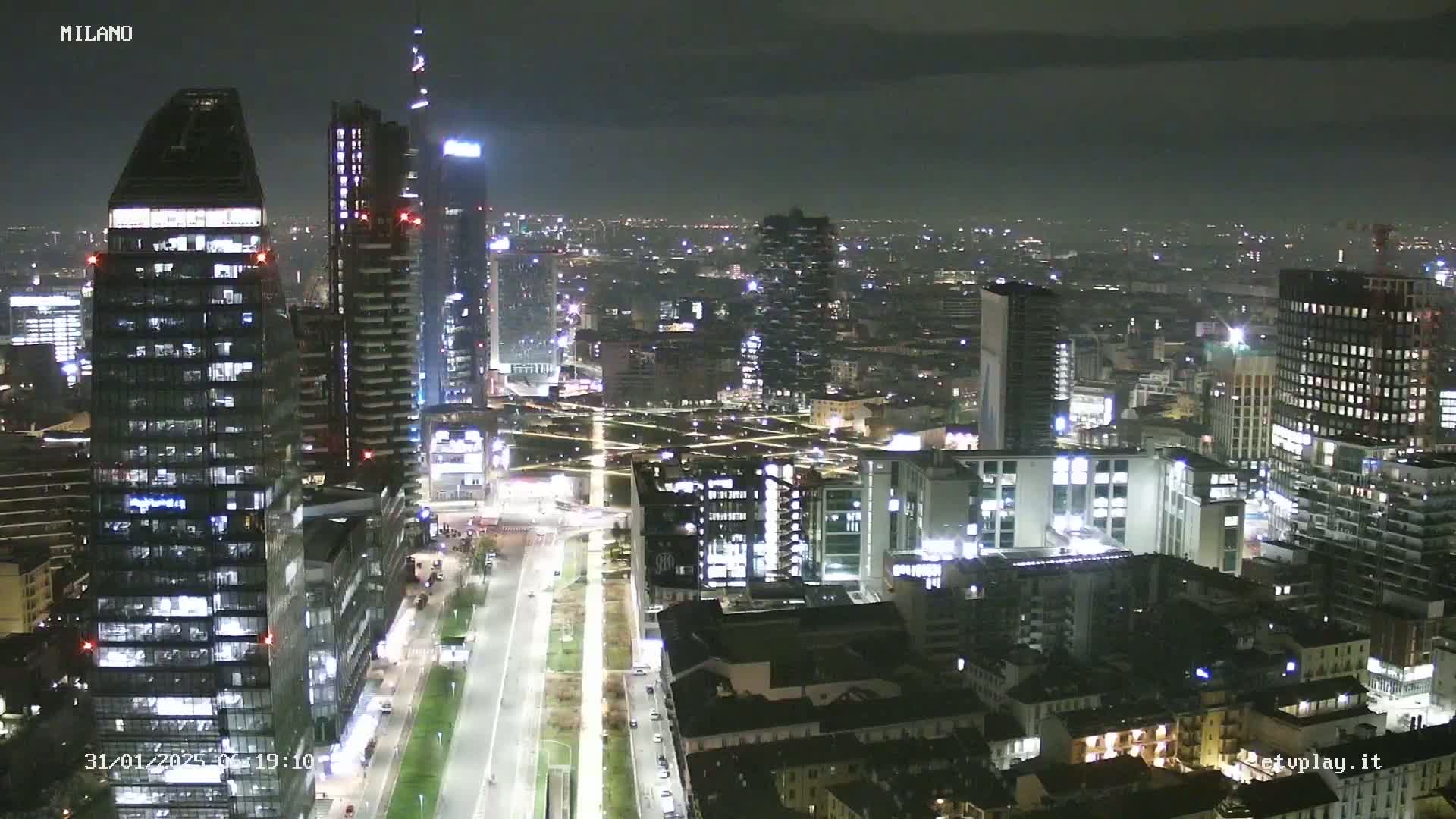 A nighttime aerial view of a city skyline with many illuminated skyscrapers and streets, under a dark sky.