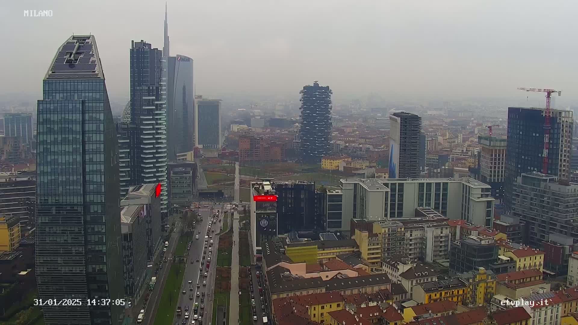 A hazy, overcast view of a densely populated city skyline featuring numerous modern skyscrapers and a wide avenue with traffic.
