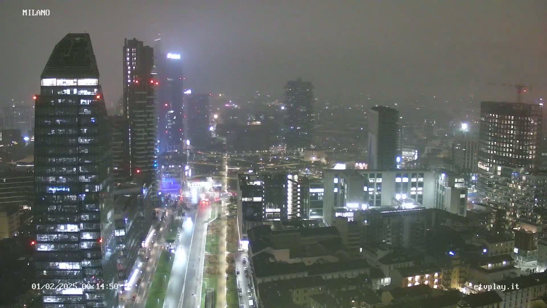 A nighttime, hazy view of a city skyline featuring numerous skyscrapers and brightly lit streets.