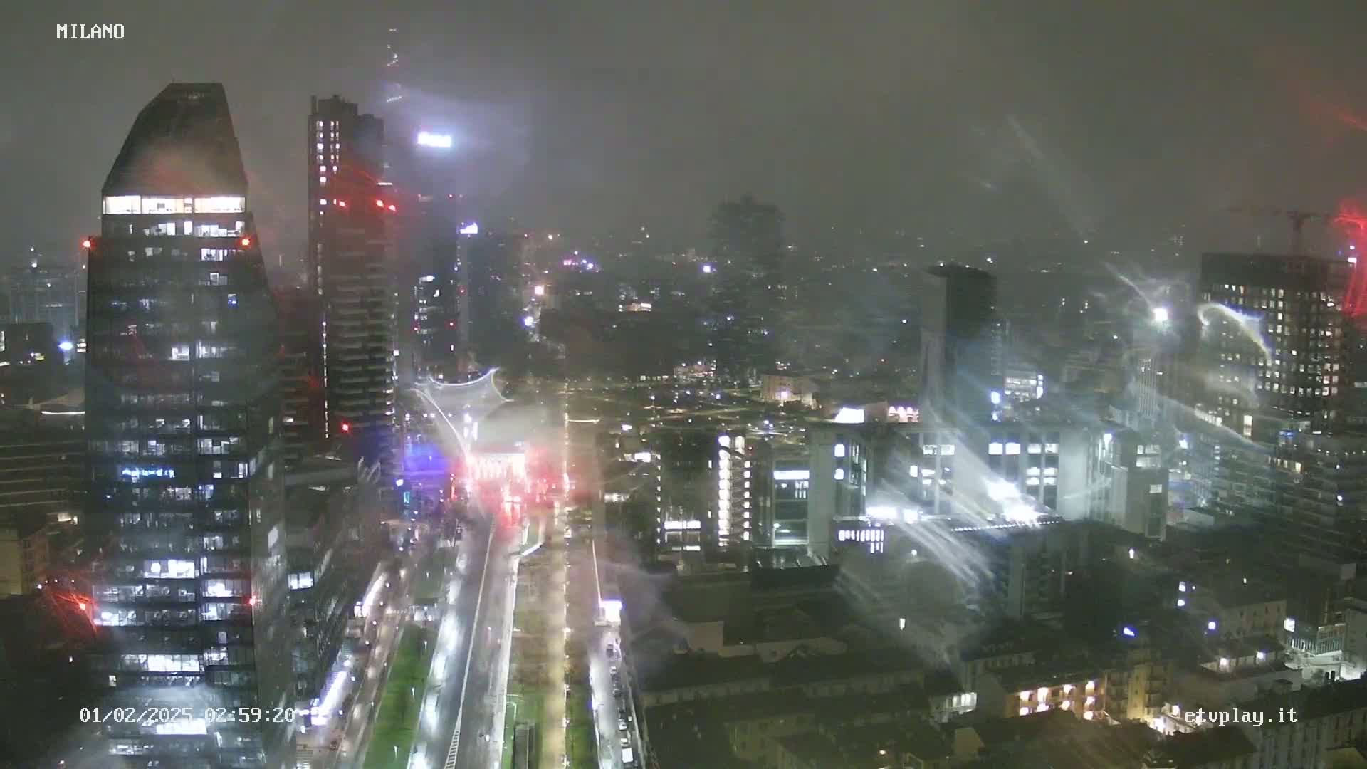 A nighttime cityscape of illuminated skyscrapers and buildings under heavy rain and wind.