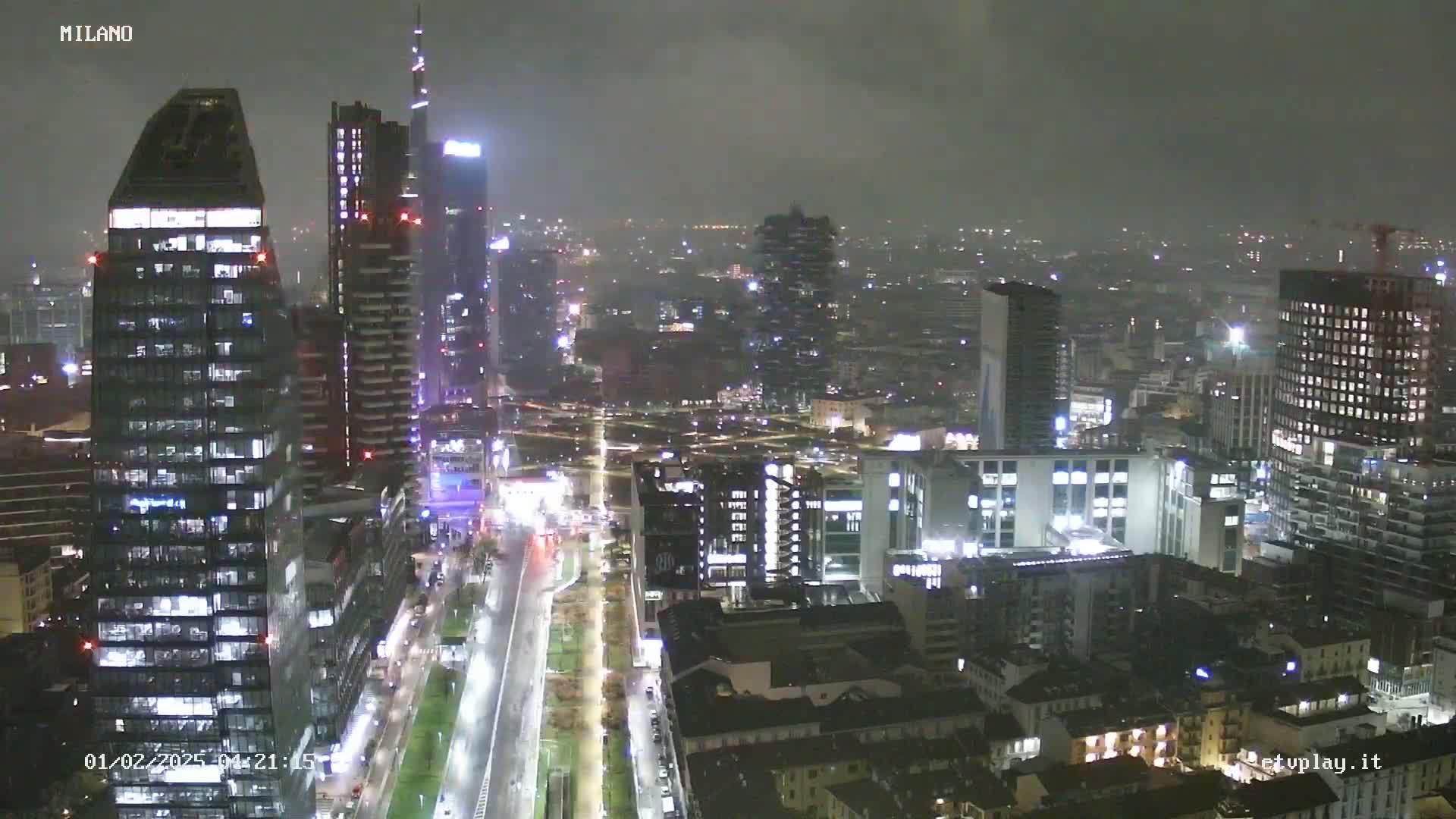 A nighttime aerial view of a city skyline with many illuminated skyscrapers under foggy or overcast conditions.