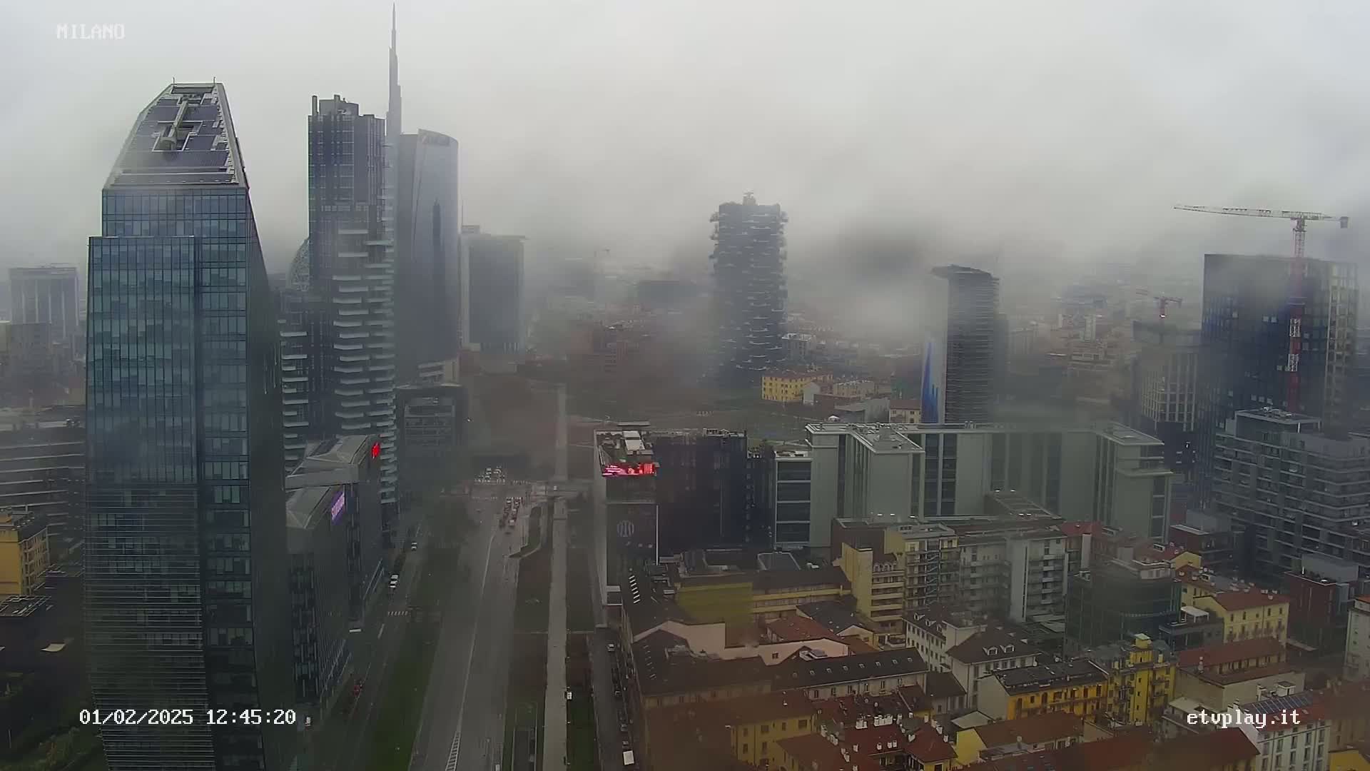 A foggy city skyline with many tall buildings and a street below, viewed from above.