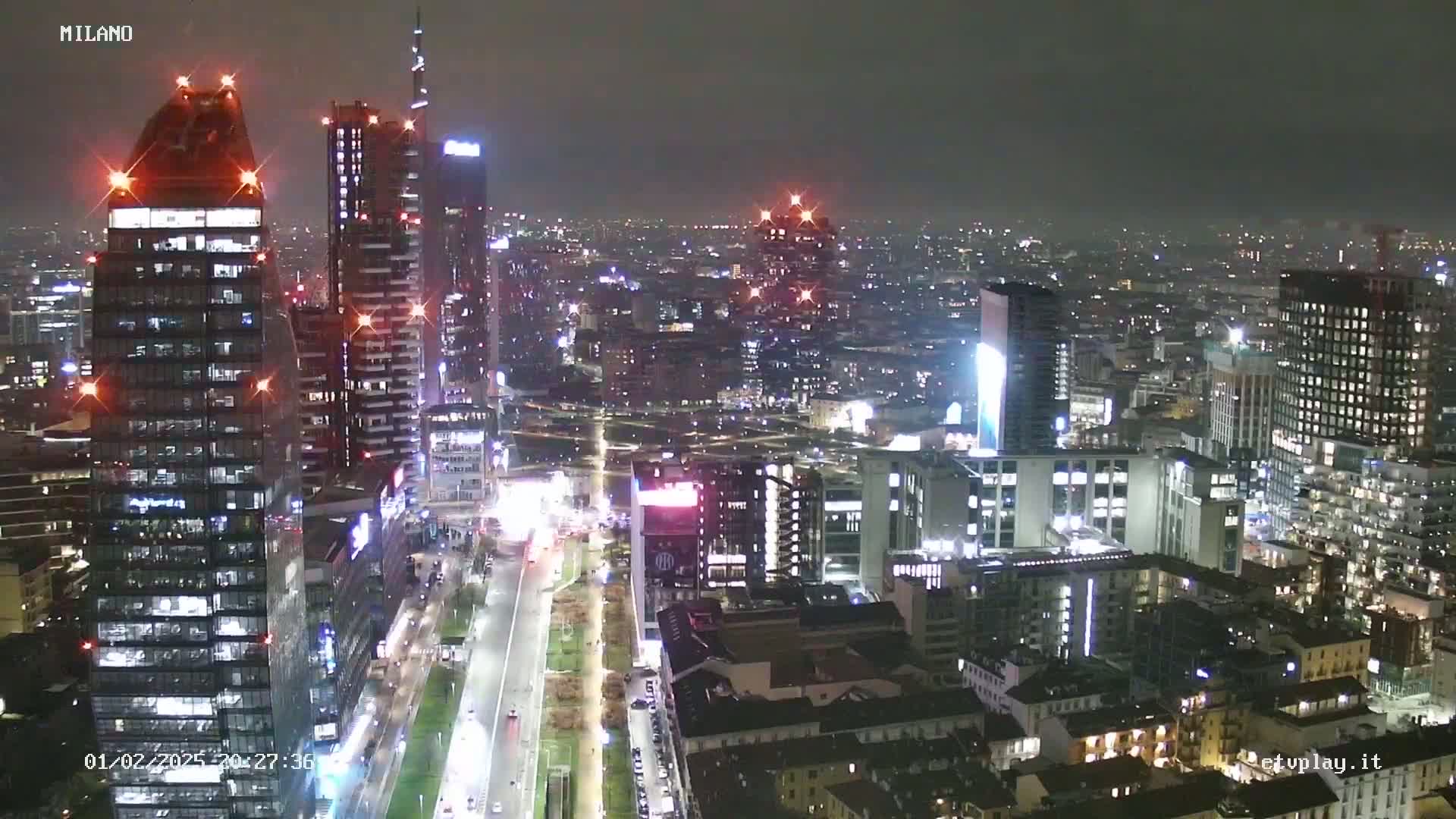 A nighttime aerial view of a city skyline showing numerous skyscrapers and city lights under a dark, slightly hazy sky.