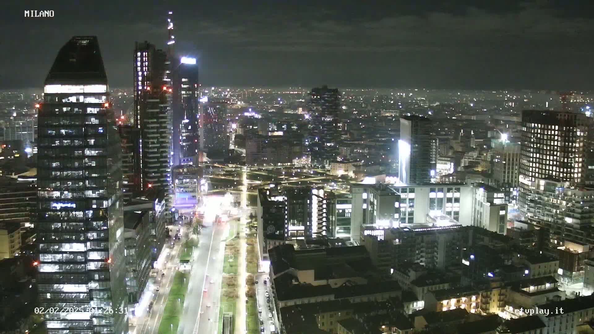 A nighttime aerial view of a city skyline with many illuminated skyscrapers and streets, under a mostly clear sky.