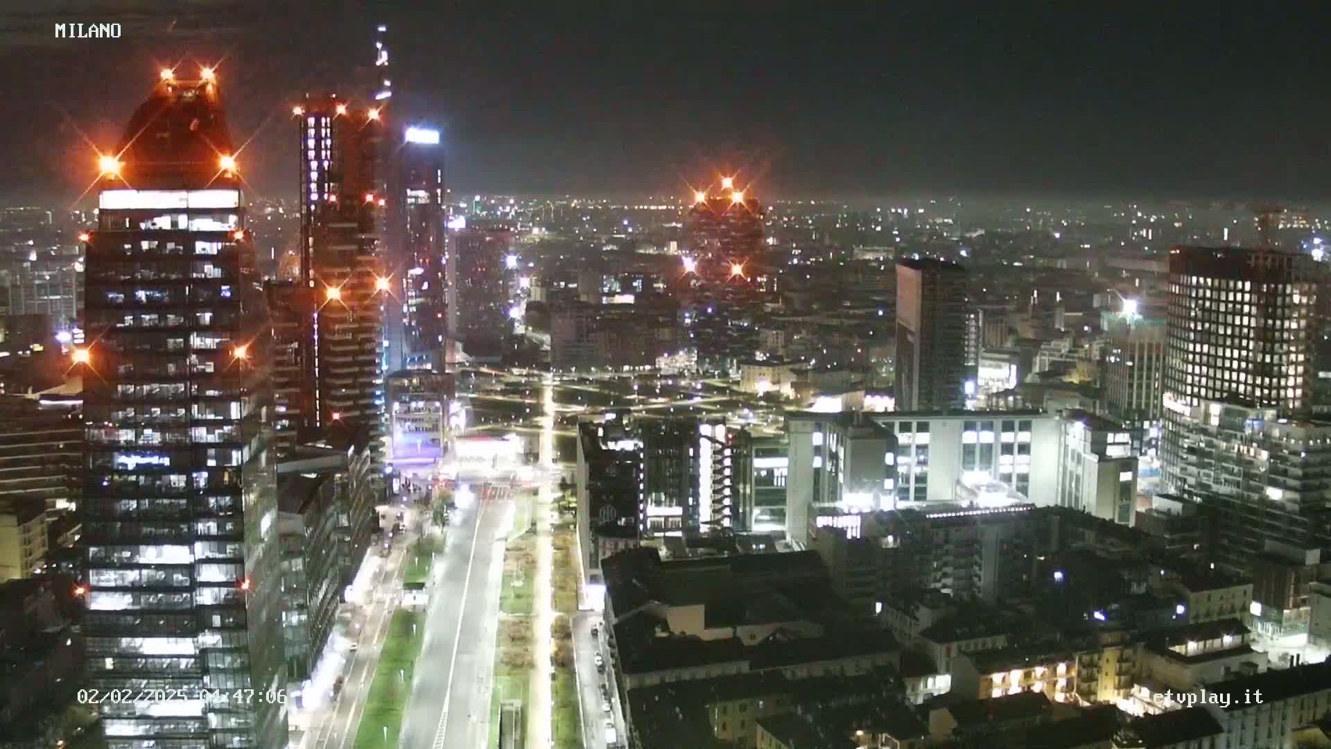 A nighttime aerial view of a city with many brightly lit skyscrapers and buildings, showing a clear night sky.