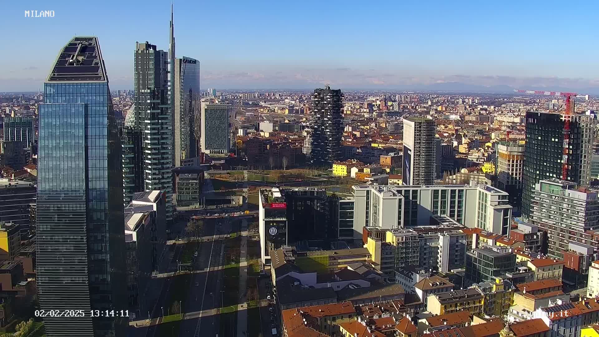 An aerial view of a densely populated city with numerous skyscrapers under a clear, sunny sky.