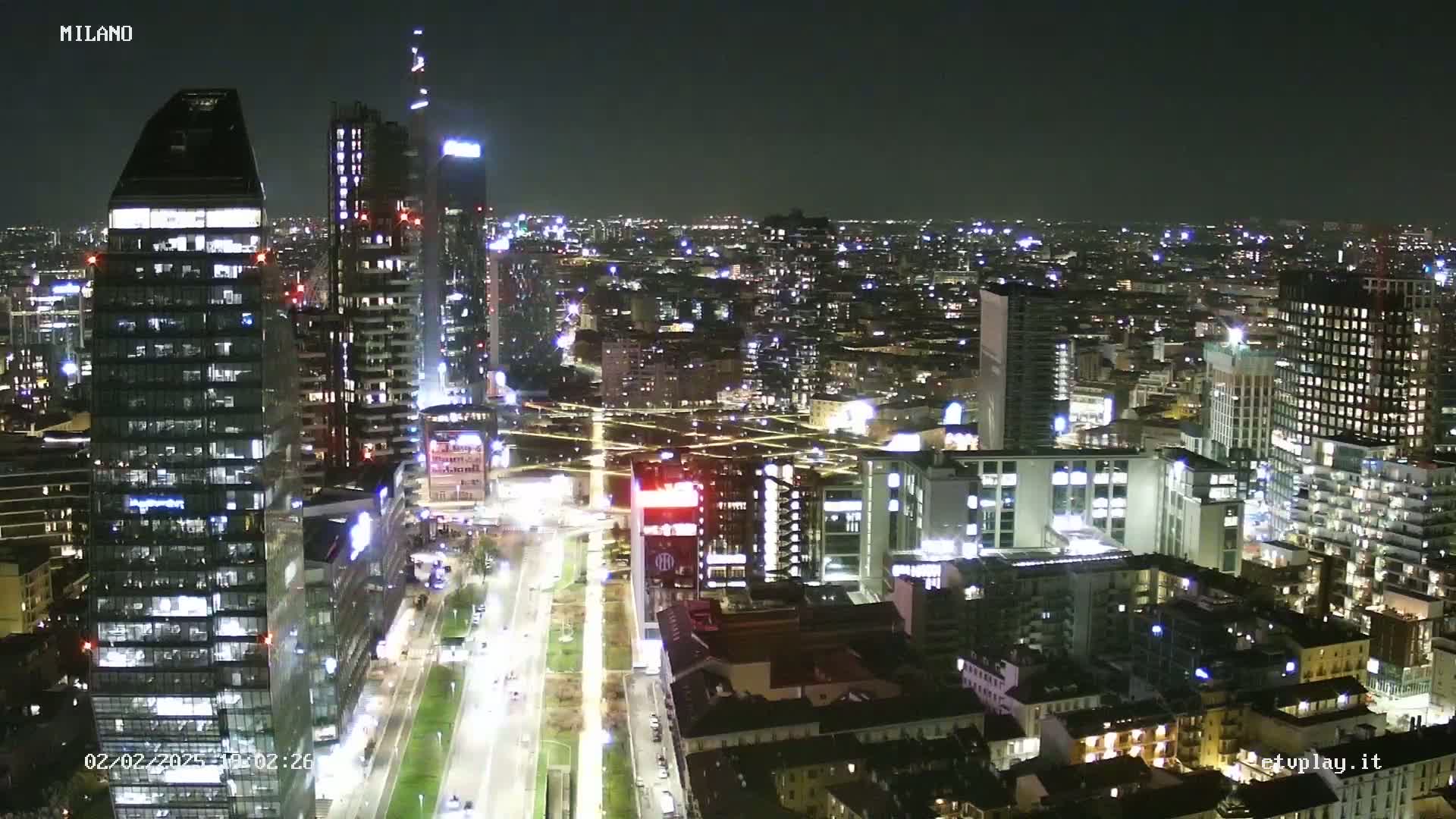 A nighttime aerial view of a city's illuminated skyline, featuring numerous skyscrapers and brightly lit streets.
