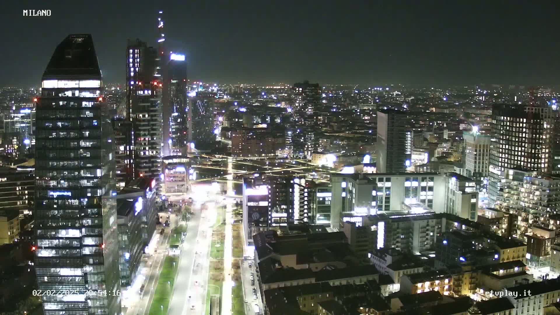 A nighttime aerial view of a city with numerous illuminated skyscrapers and buildings, showing a clear sky.