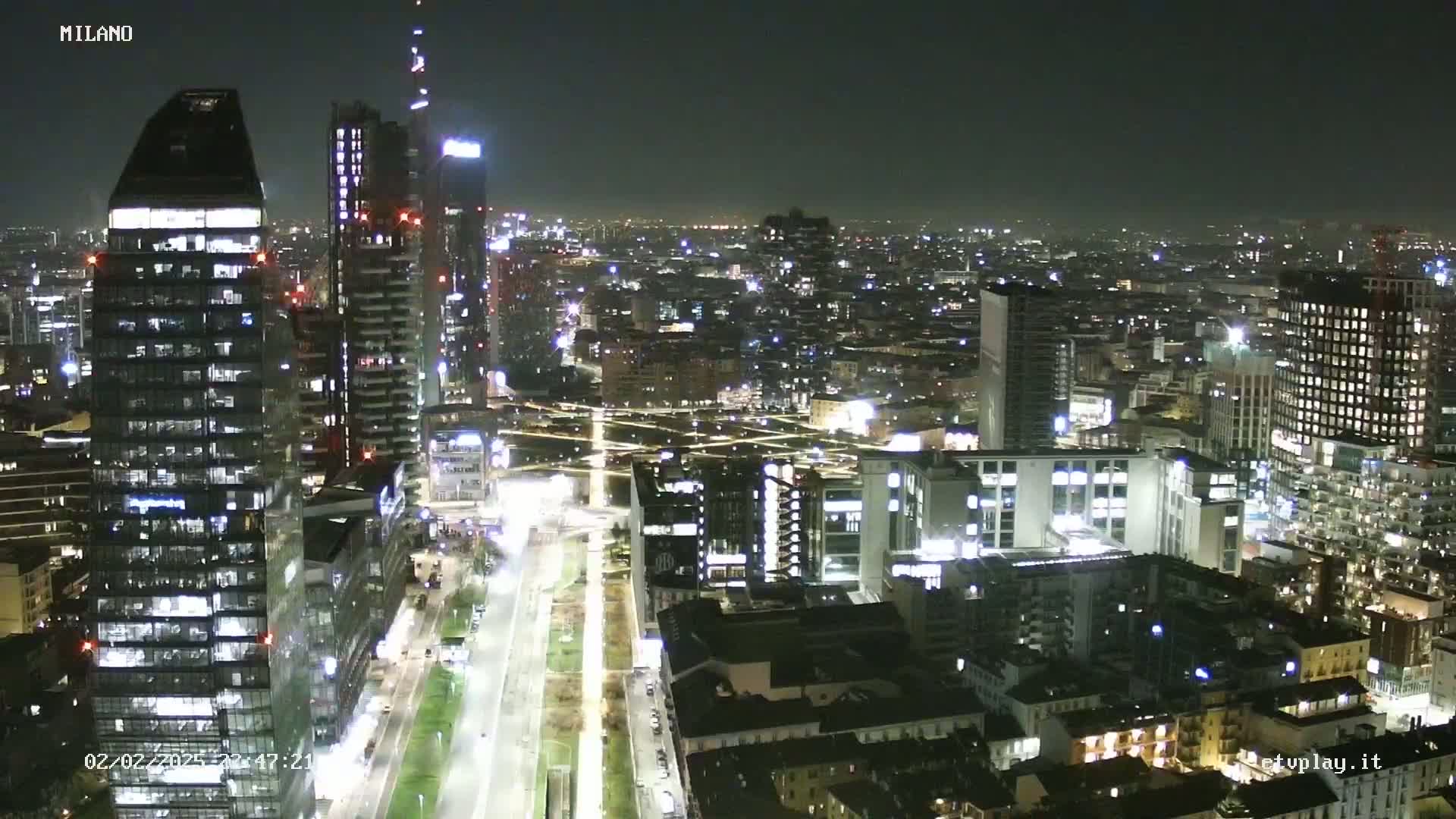 A nighttime aerial view of a city, showing numerous illuminated buildings and streets, under a clear sky.