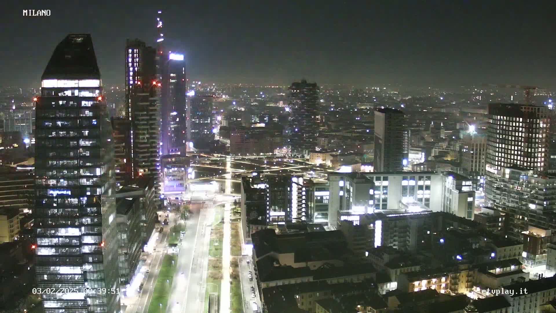 A nighttime aerial view of a city, showing numerous illuminated buildings and streets, under a clear, dark sky.
