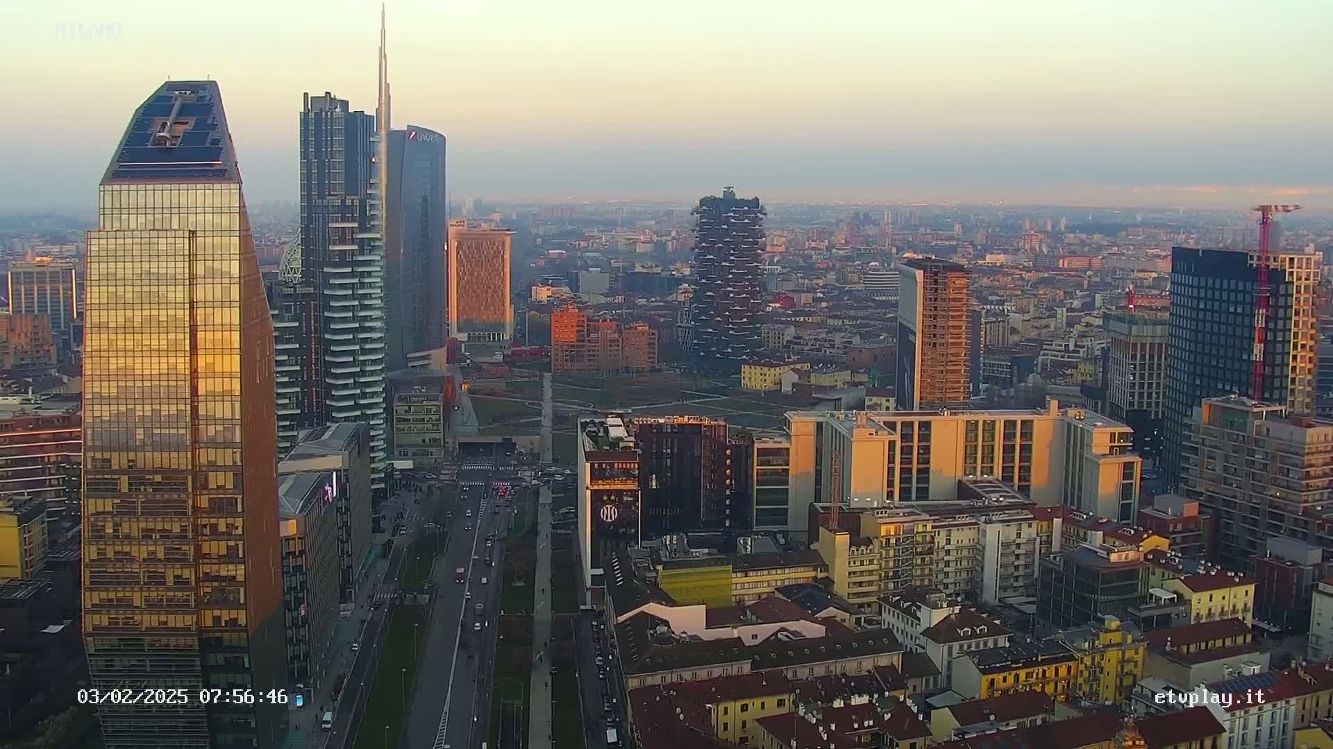 An aerial view of a city skyline at sunset, showing numerous skyscrapers and surrounding buildings under a clear sky.